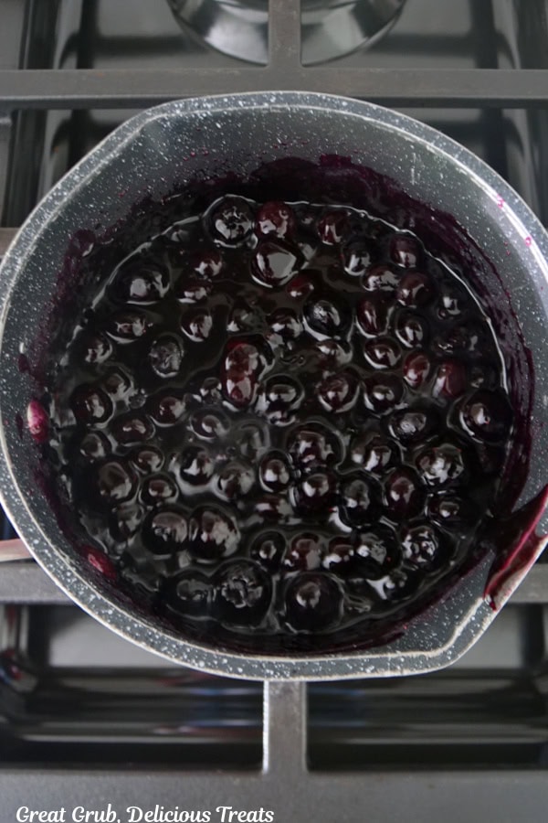 A saucepan with blueberries cooking on the stove.