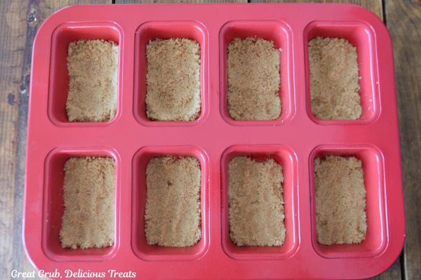 A red mini loaf pan with brown sugar packed into all the little loaf spaces.