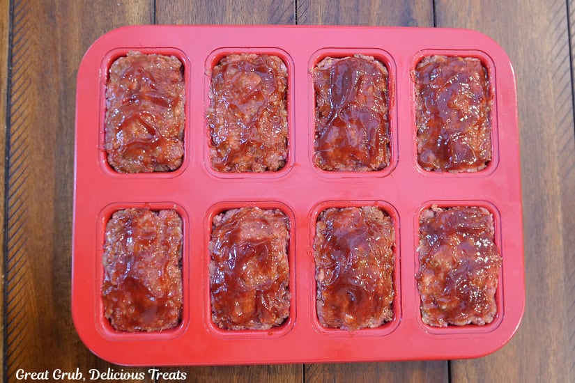 A red mini loaf pan with the mini meatloaves in it topped with a barbecue ketchup topping.