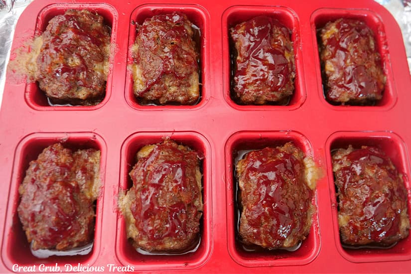 A red mini loaf pan with 8 cooked mini meatloaves in it after being removed from the oven.