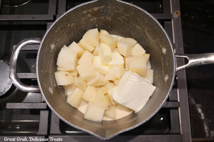 A saucepan with the cooked potatoes and the cream cheese, butter, and evaporated milk added to the pan before being mashed together.
