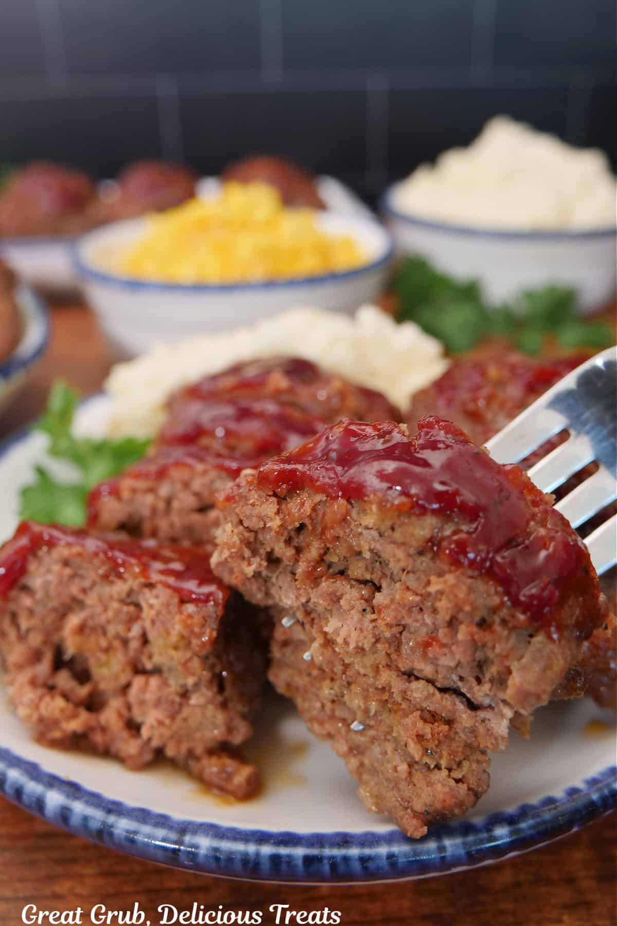 A sliced mini meatloaf on a white plate with blue trim and a bite on a fork.