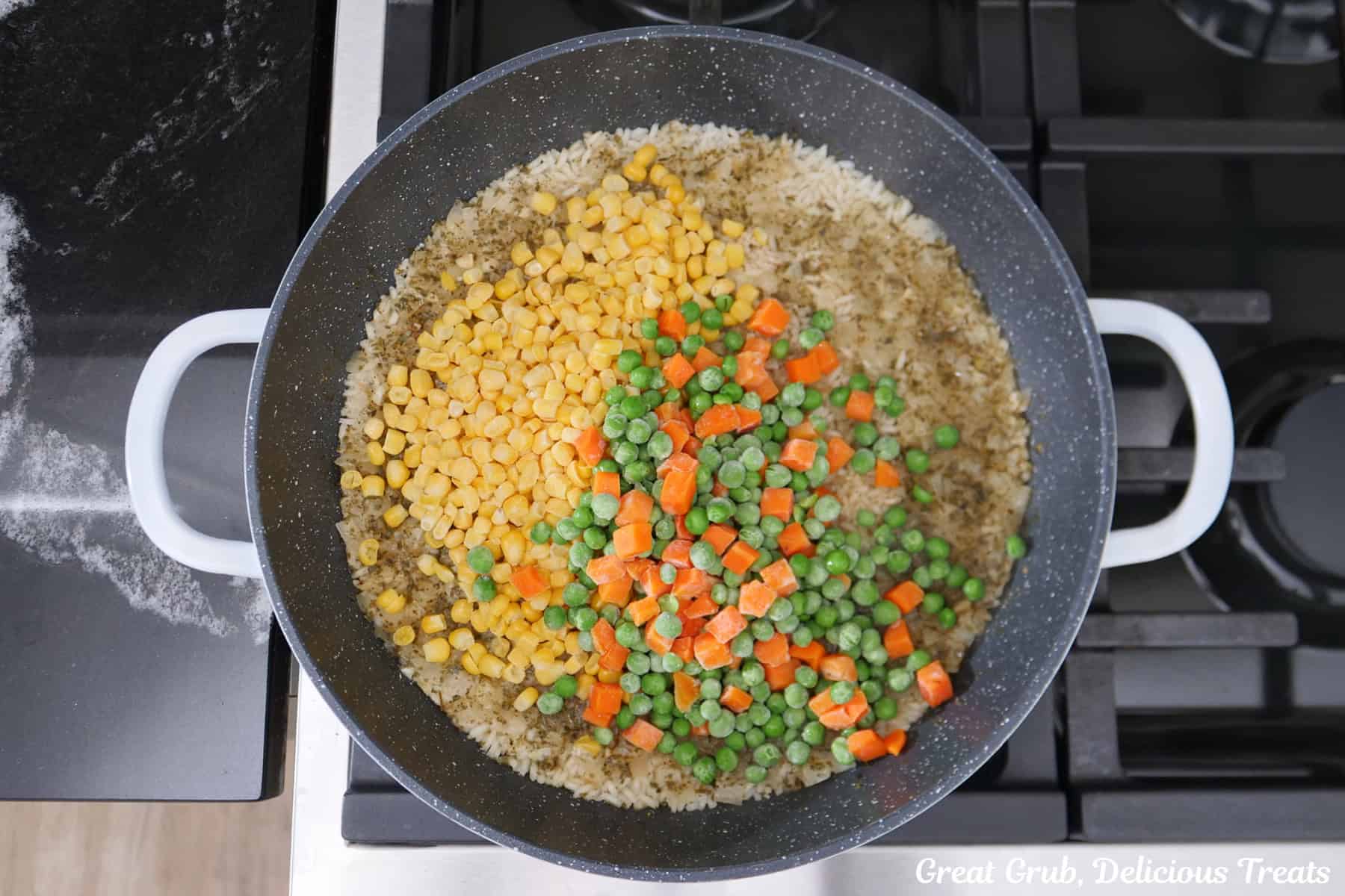 A pan with rice, onions, garlic, broth, seasonings, and frozen vegetables added before mixing everything together.