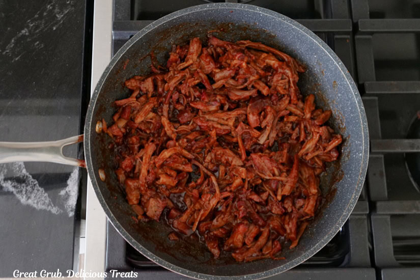 A sauce pan on the stovetop with leftover pulled pork and barbecue sauce all mixed together.