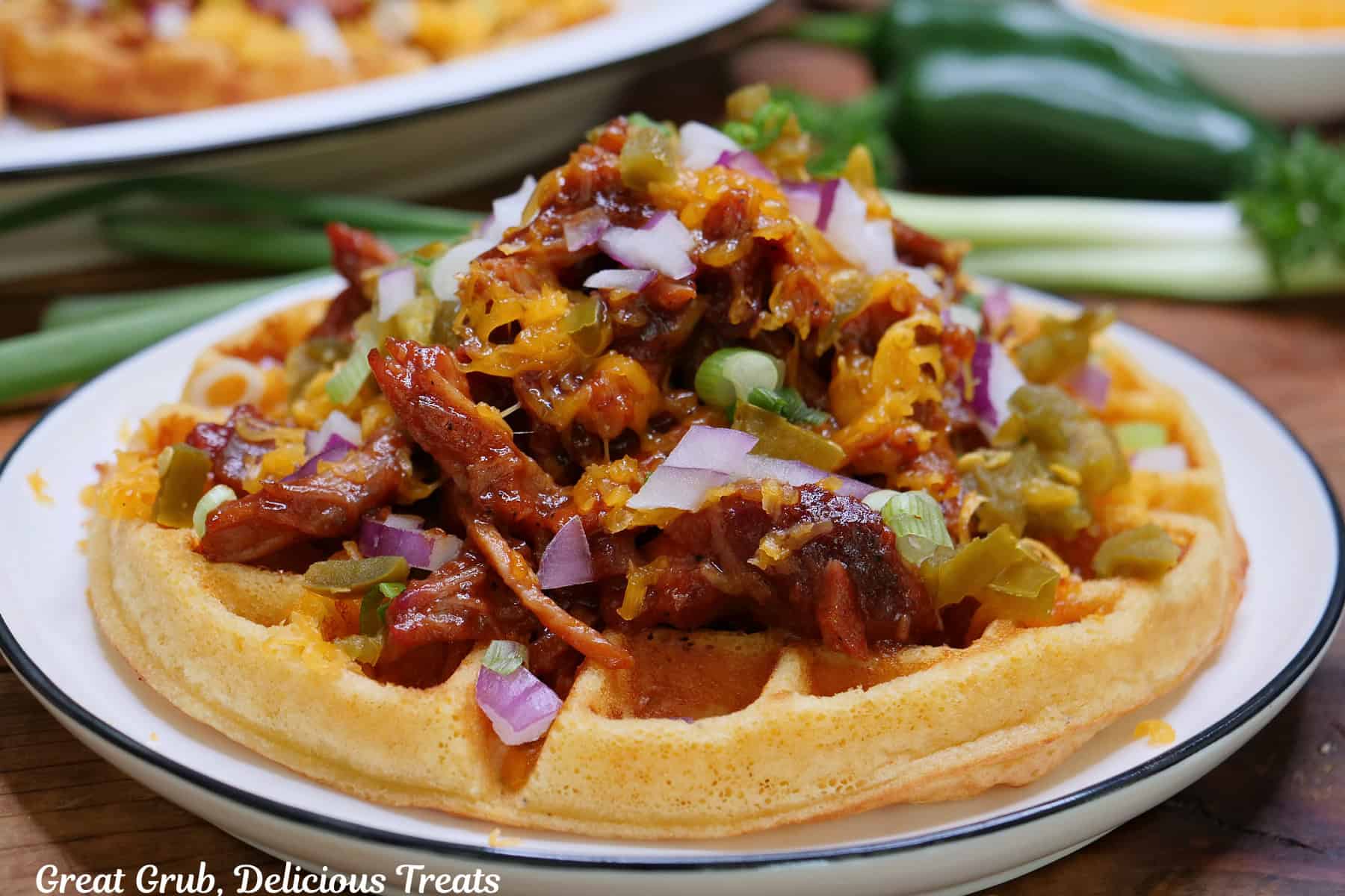 A round white plate with blue trim with a cornbread waffle topped with shredded pulled pork, cheese, onions, and drizzled with barbecue sauce.