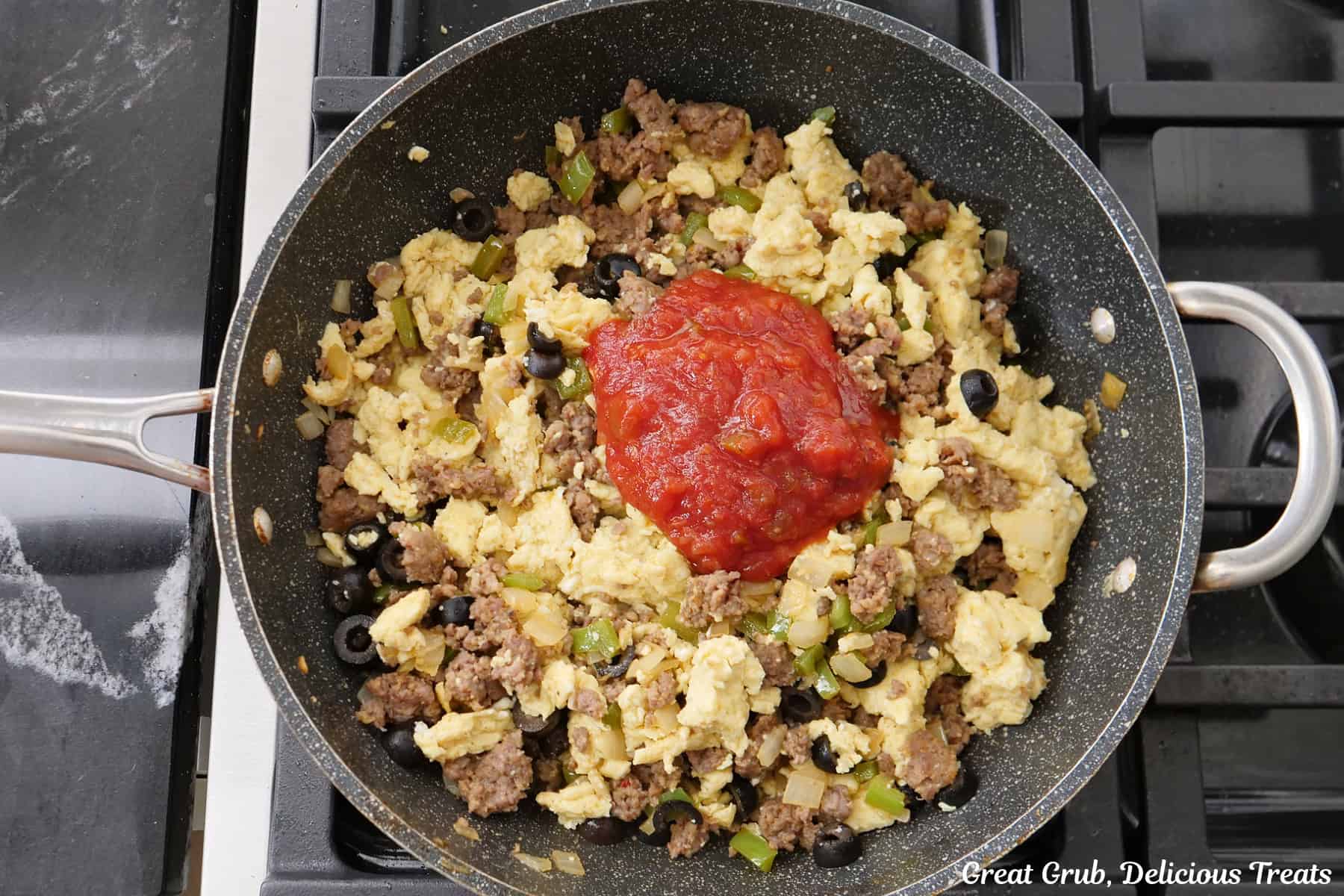 A frying pan with cooked sausage, scrambled eggs, onions, peppers, and salsa added to it.