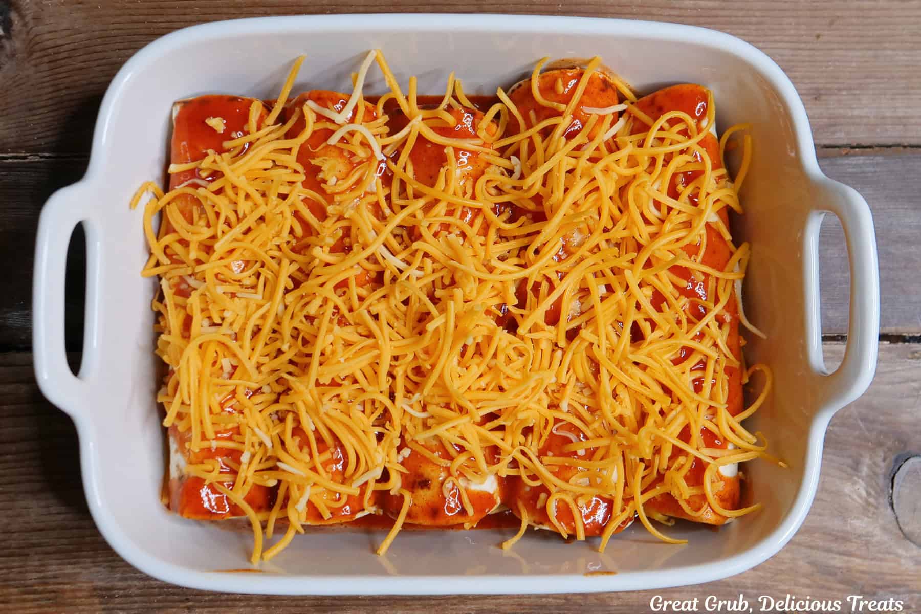 A white baking dish with five sausage breakfast enchiladas in it and about to be put in the oven to bake.