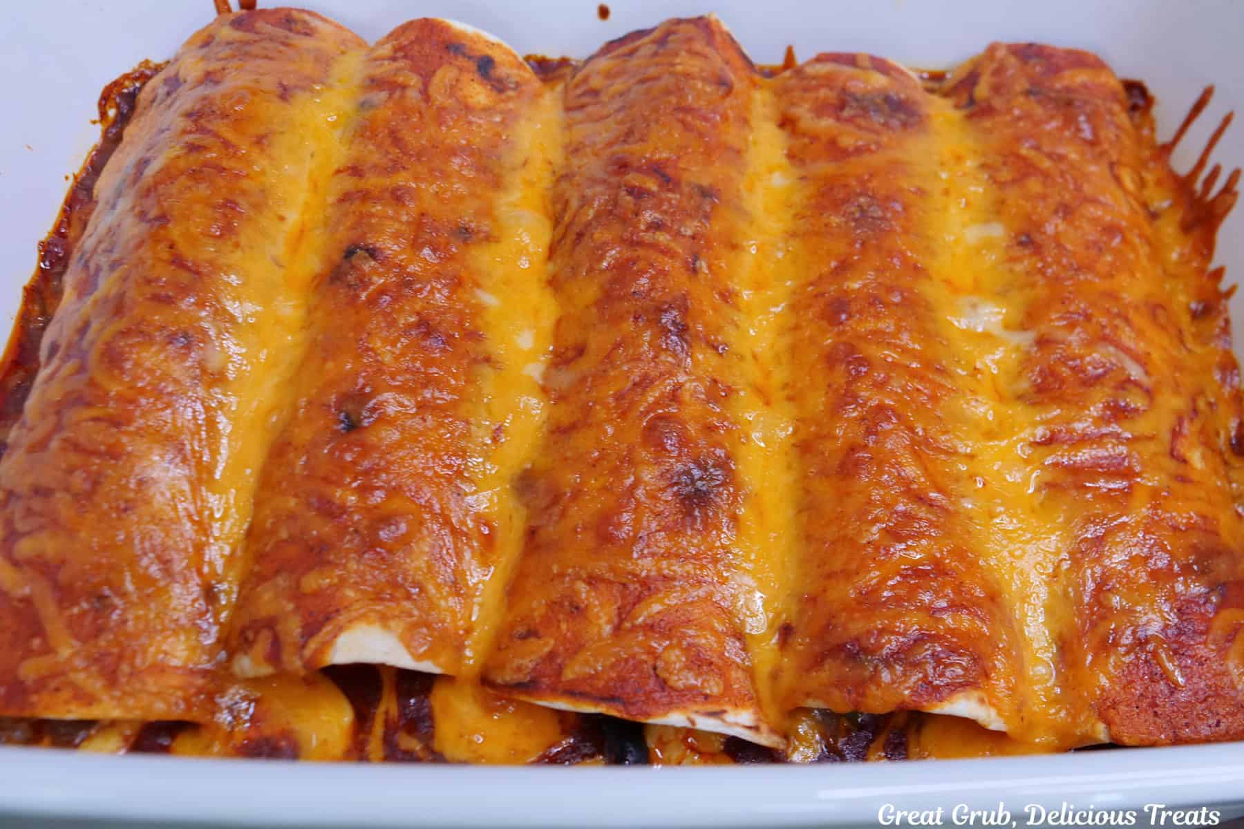 A white baking dish with baked sausage breakfast enchiladas in it right after being removed from the oven.
