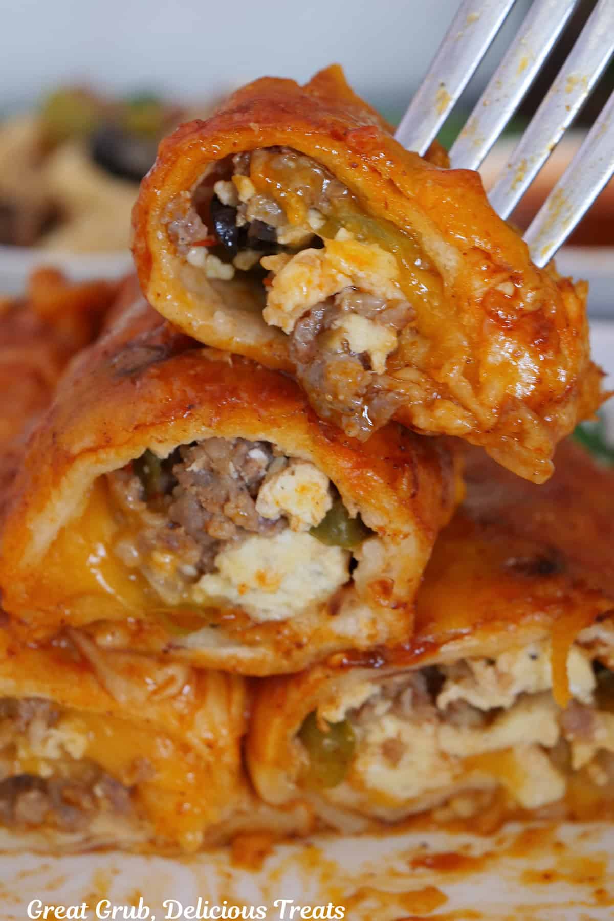 A bite of a breakfast enchilada on a fork with two more enchiladas underneath on a white plate.