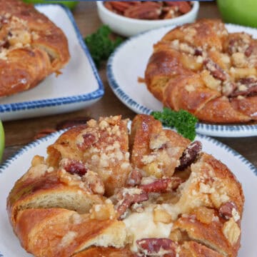 A rustic wood surface with three white plates with blue trim with an apple cheesecake croissant on each plate, and a title overlay at the top.