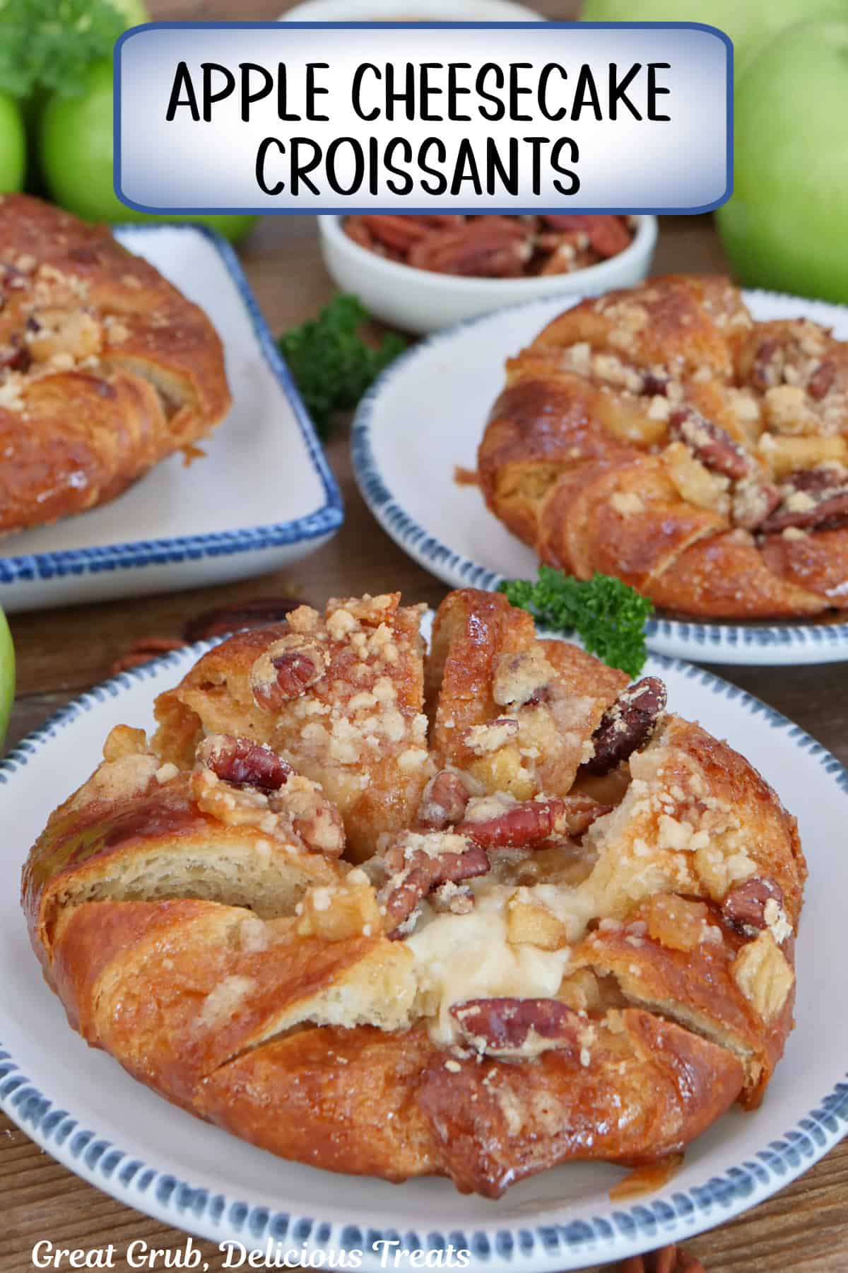 A rustic wood surface with three white plates with blue trim with an apple cheesecake croissant on each plate, and a title overlay at the top.