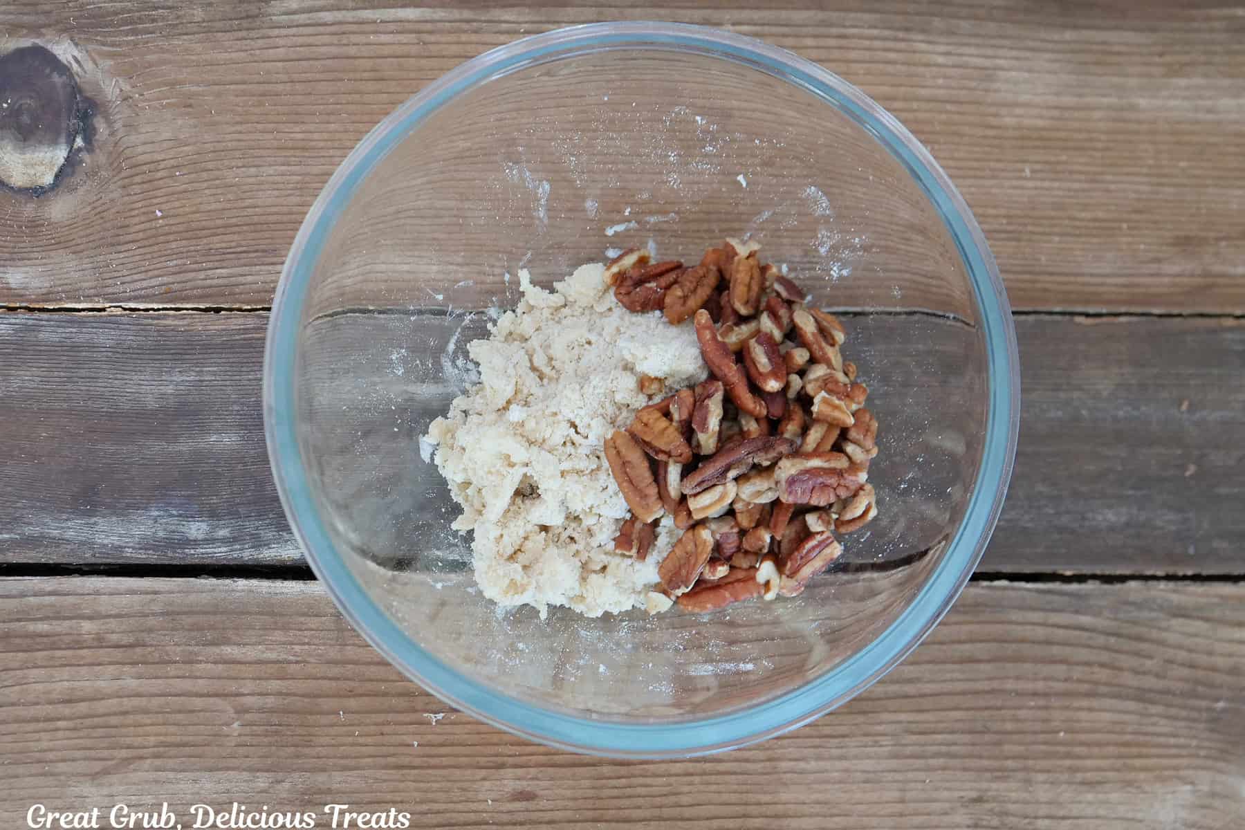 A wood surface with a glass bowl filled with the pecan crumb topping ingredients in it.