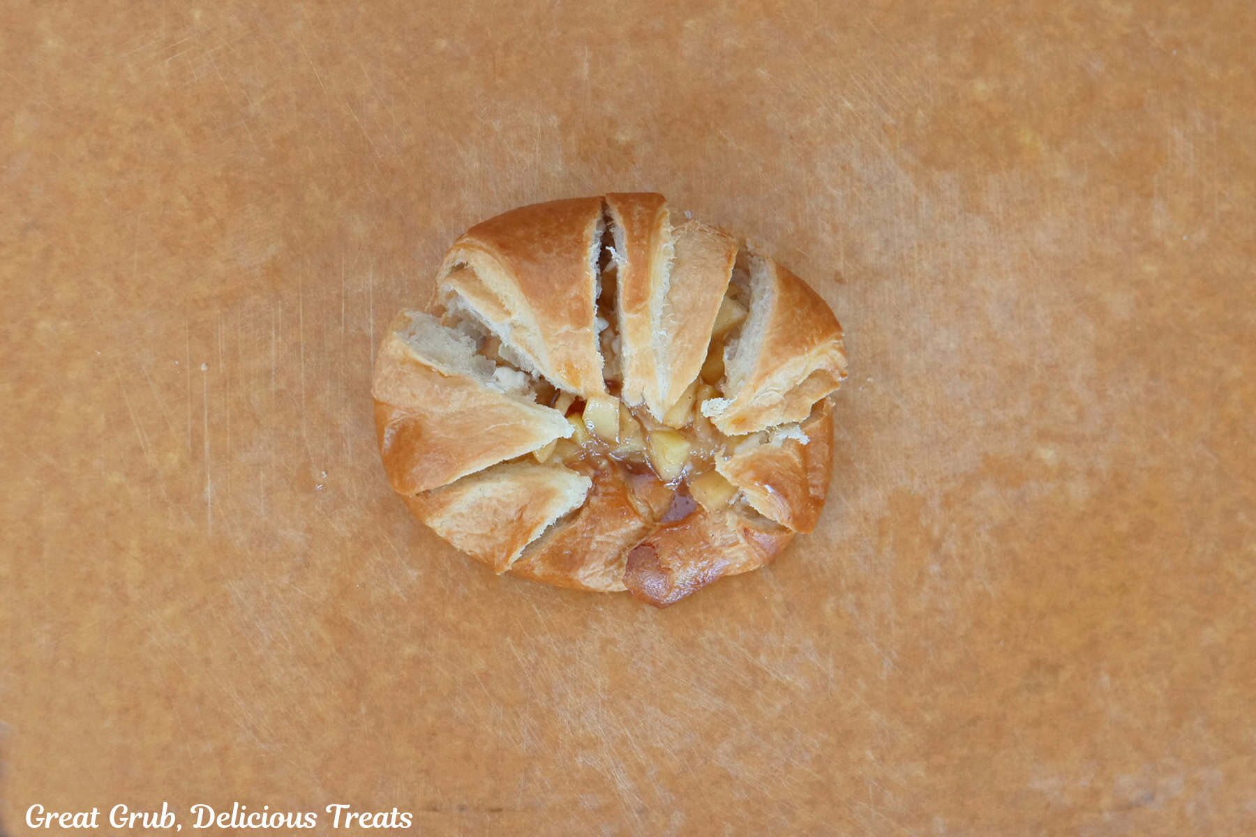 A cutting board with a single croissant on it with the cheesecake and apple filling in it.