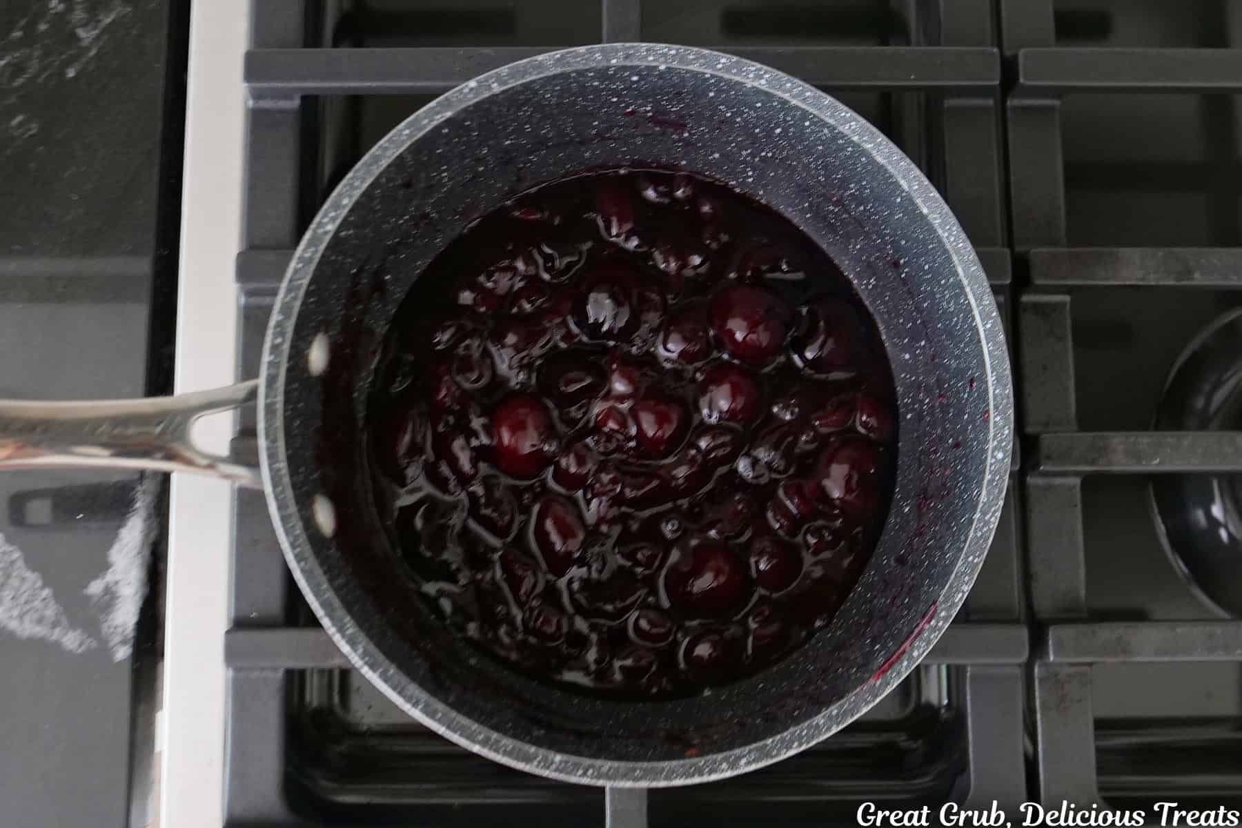 A saucepan on the stove with a cherry topping being cooked in it.