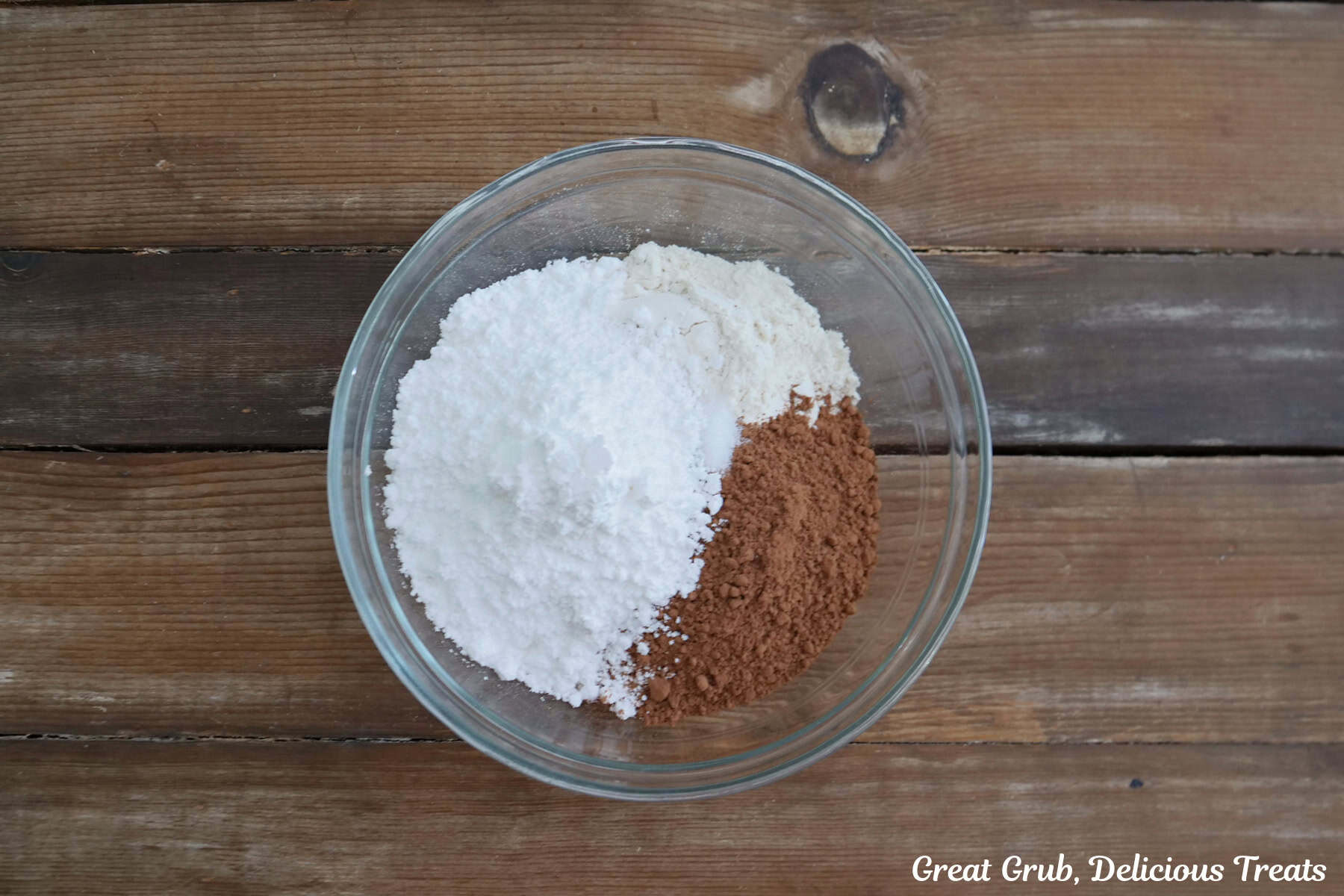 A wood surface with a glass bowl filled with the dry brownie ingredients in it.