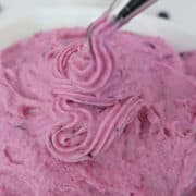 A white surface with a white bowl filled with homemade blueberry buttercream frosting, with a title overlay at the top.