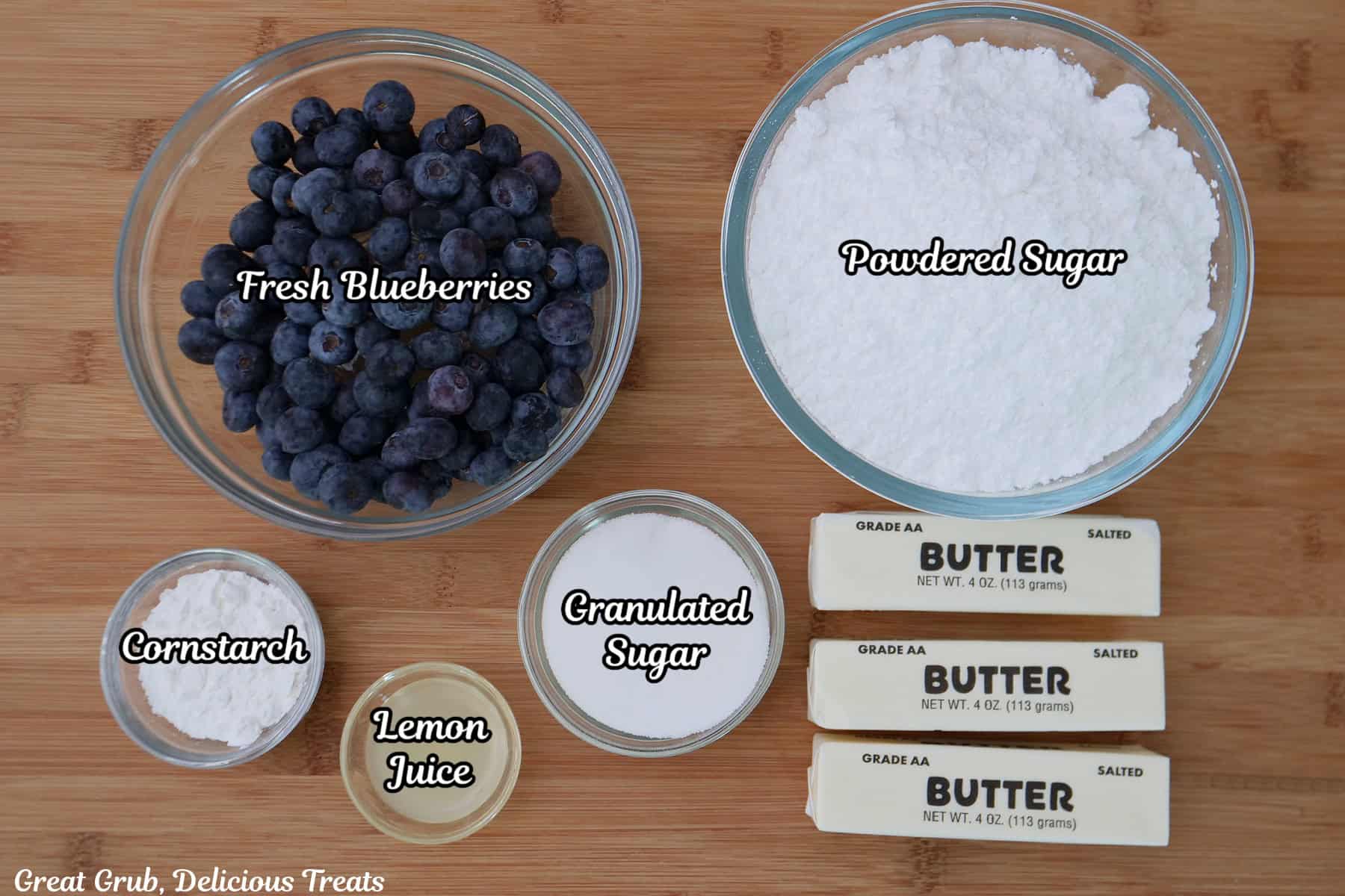 A wood surface with all the ingredients placed on it to make homemade blueberry buttercream frosting.