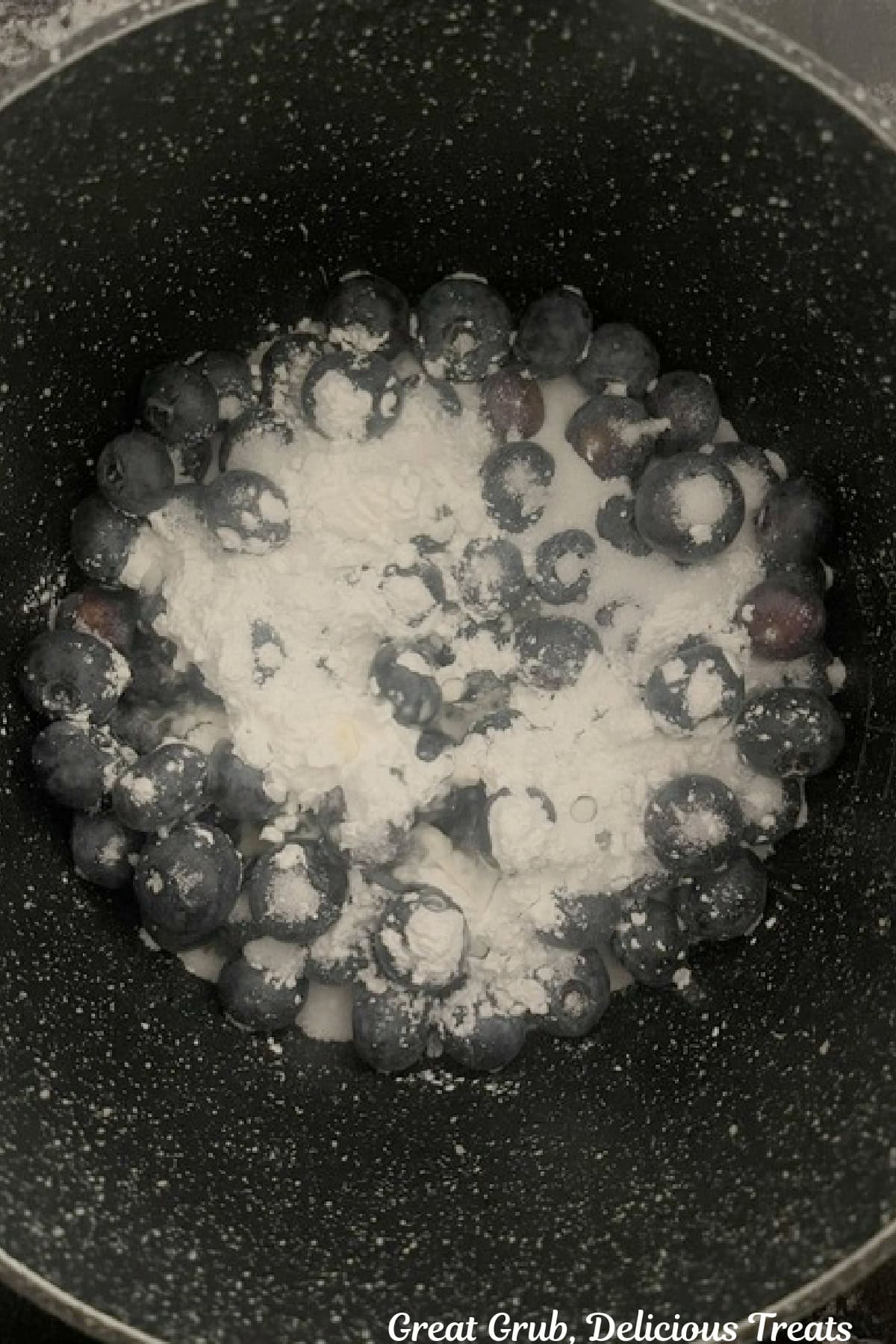 A saucepan with fresh blueberries, sugar, cornstarch, and lemon juice in it before being heated and made into sauce.