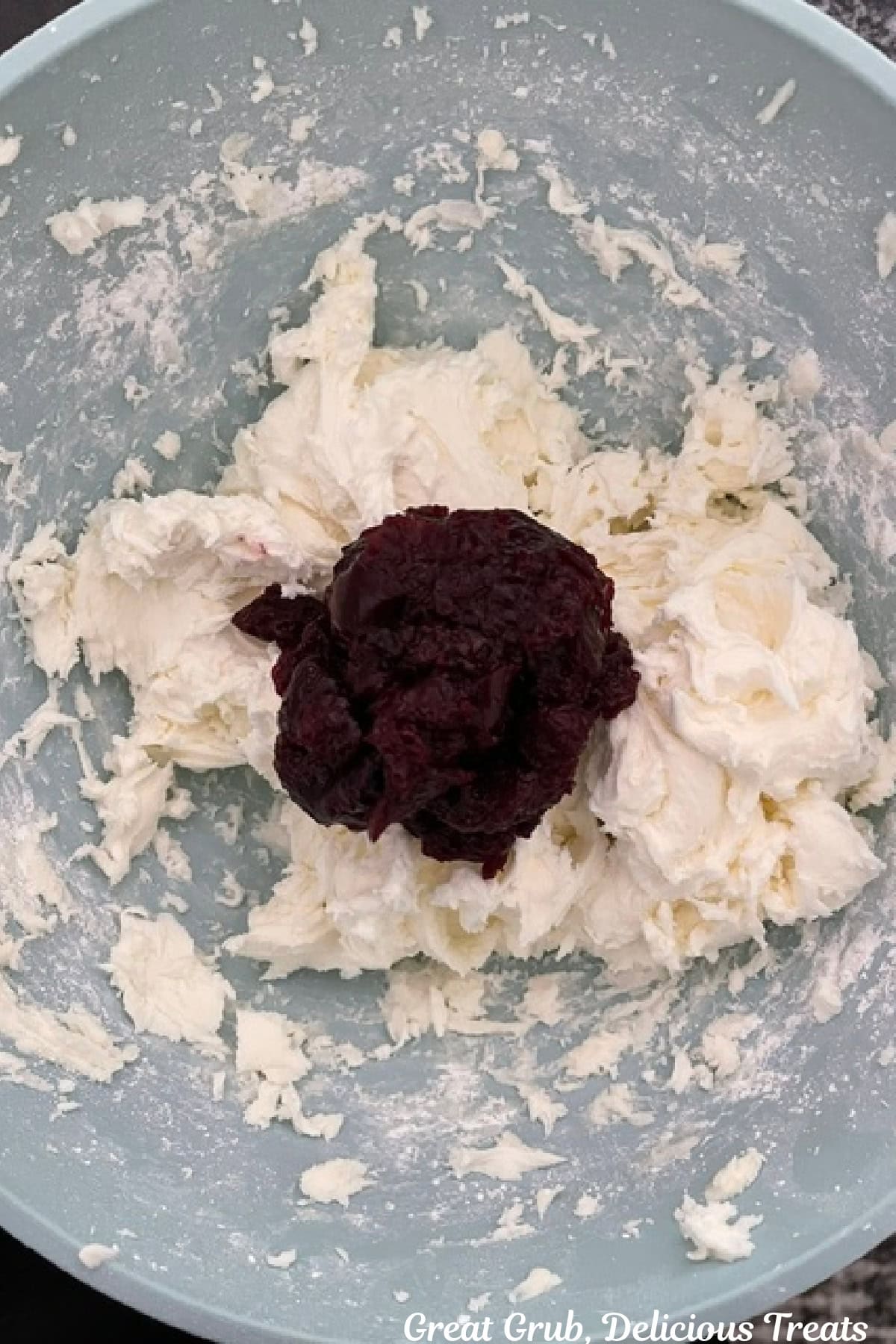 A light blue bowl with buttercream frosting and blueberry sauce added before being mixed together.