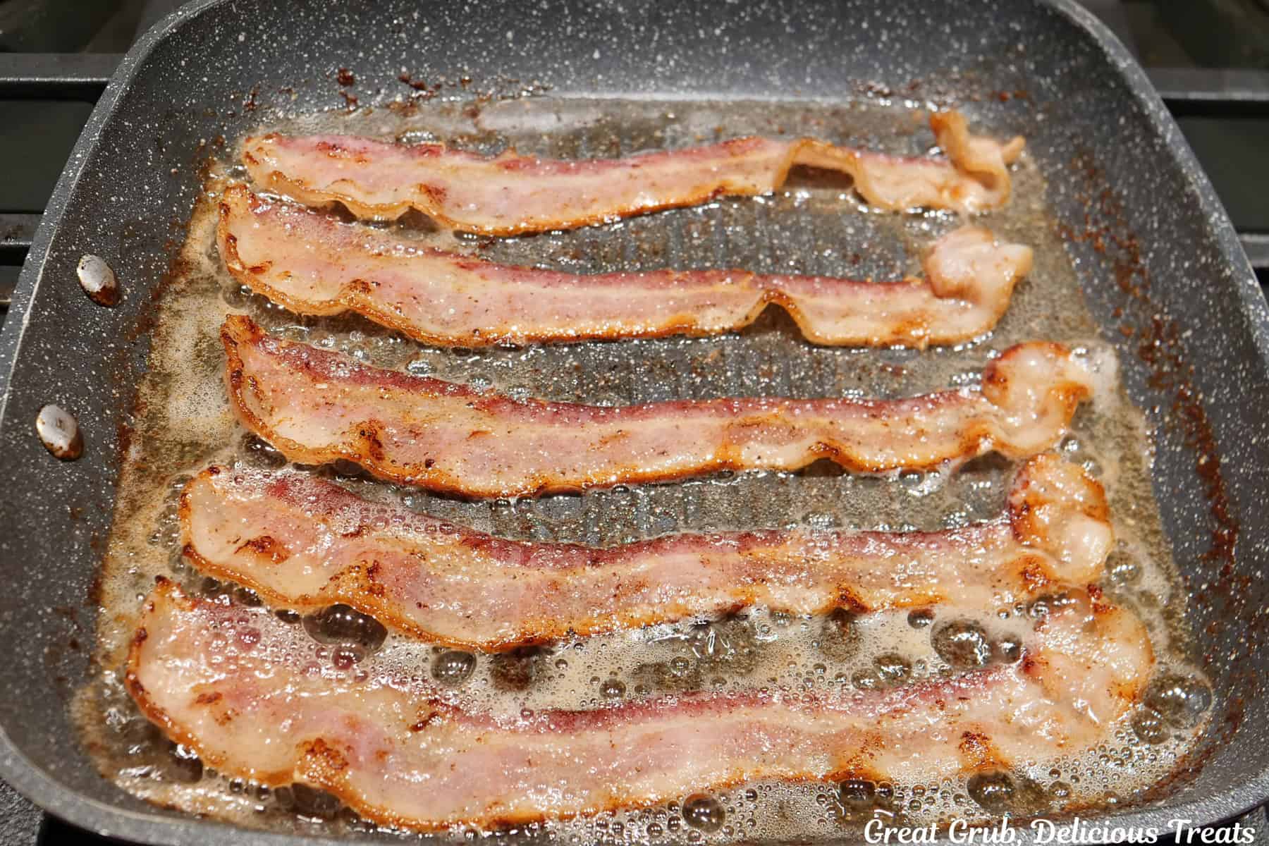 A frying pan on the stove with five strips of bacon frying in the pan.