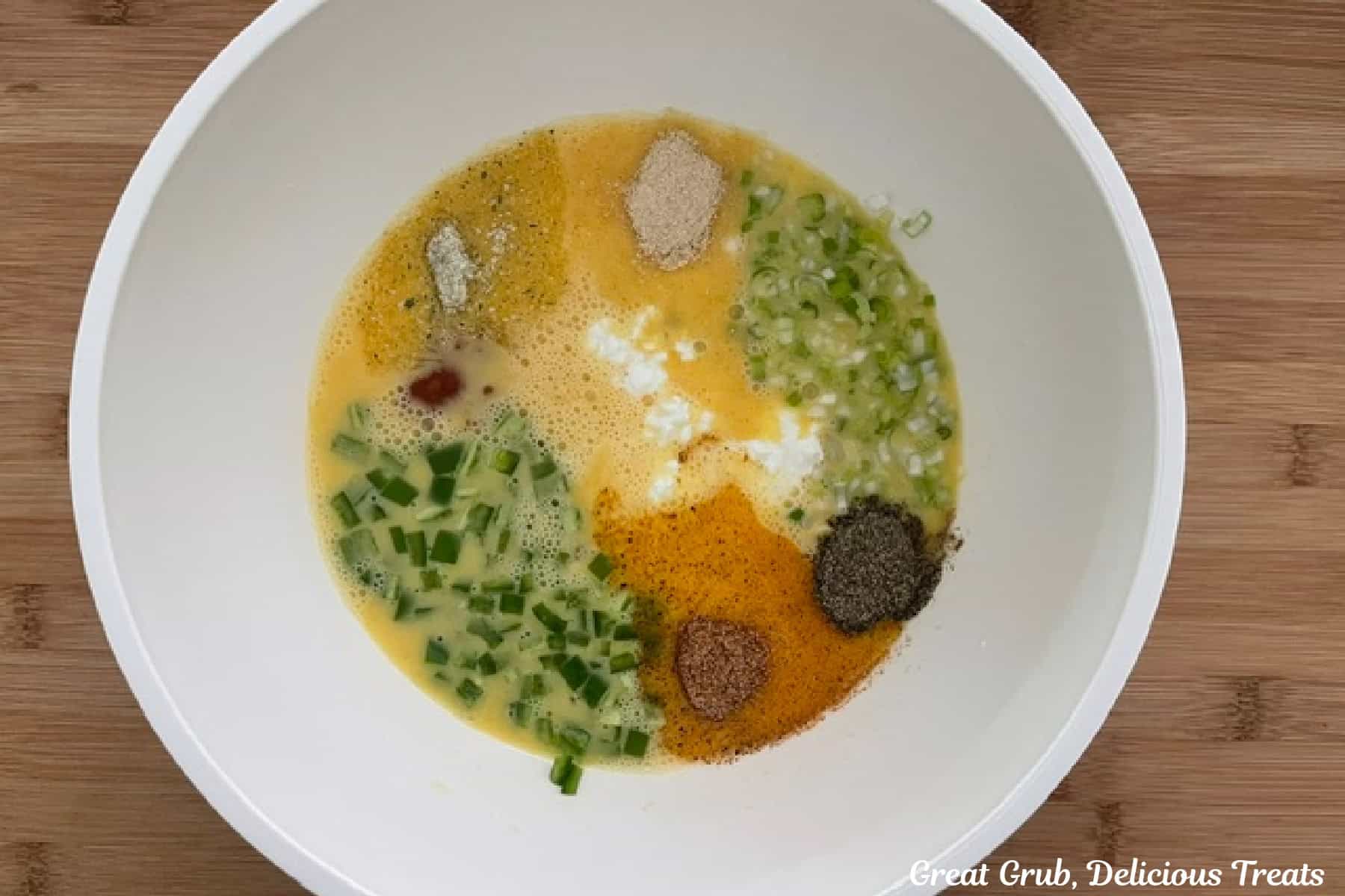 A wood surface with a white bowl filled with eggs, seasonings, jalapeno, green onions, and cottage cheese in it.