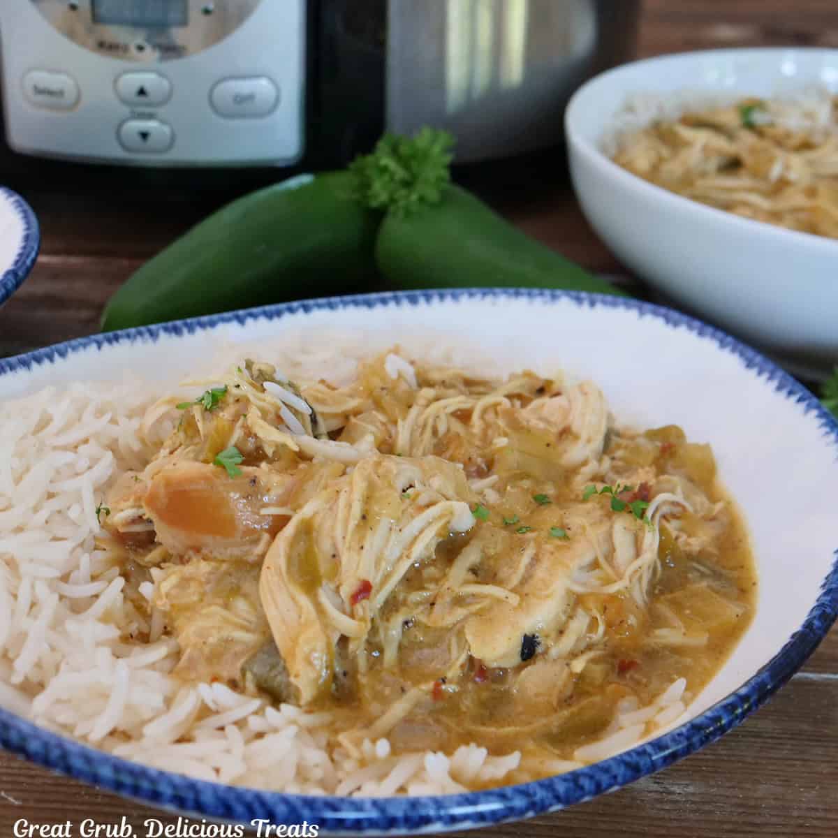 A wood surface with a white bowl with blue trim filled with a serving of spicy queso chicken shredded and served on white rice.