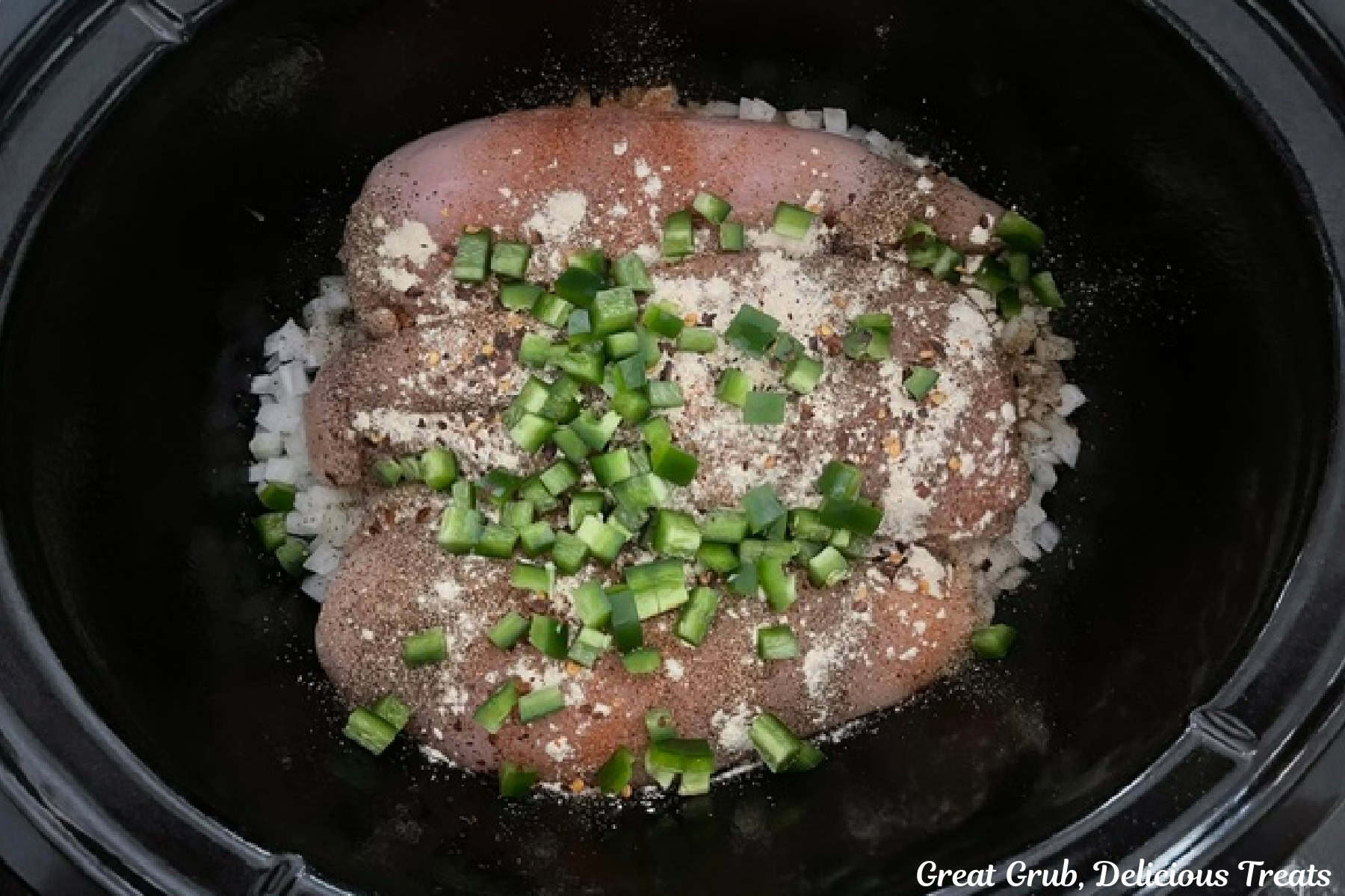 A black crock pot filled with diced onions, three chicken breasts, seasonings, and diced jalapenos.
