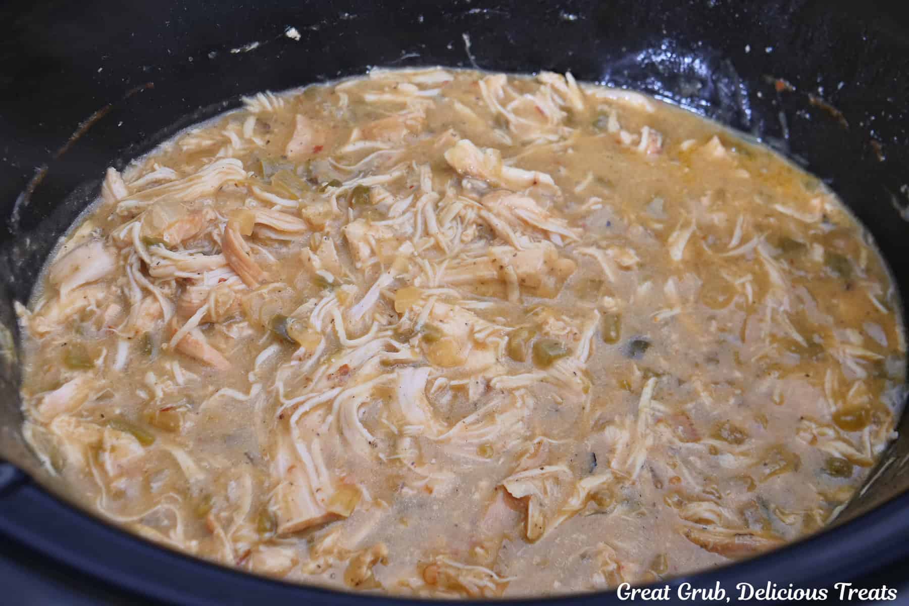 A black crock pot with shredded spicy queso chicken in it.