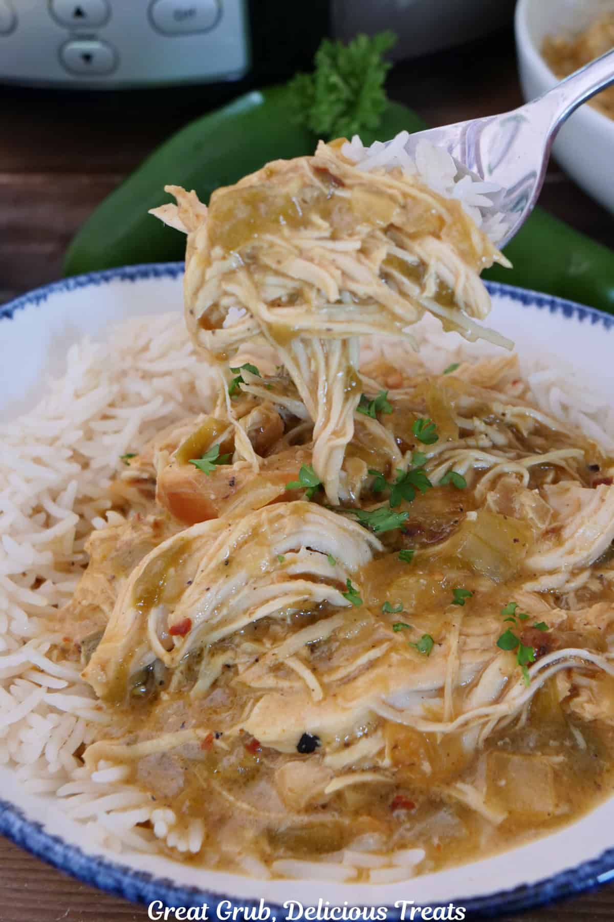 A white bowl with blue trim filled with white rice and shredded spicy queso chicken in it with a bite on a fork held above the bowl.