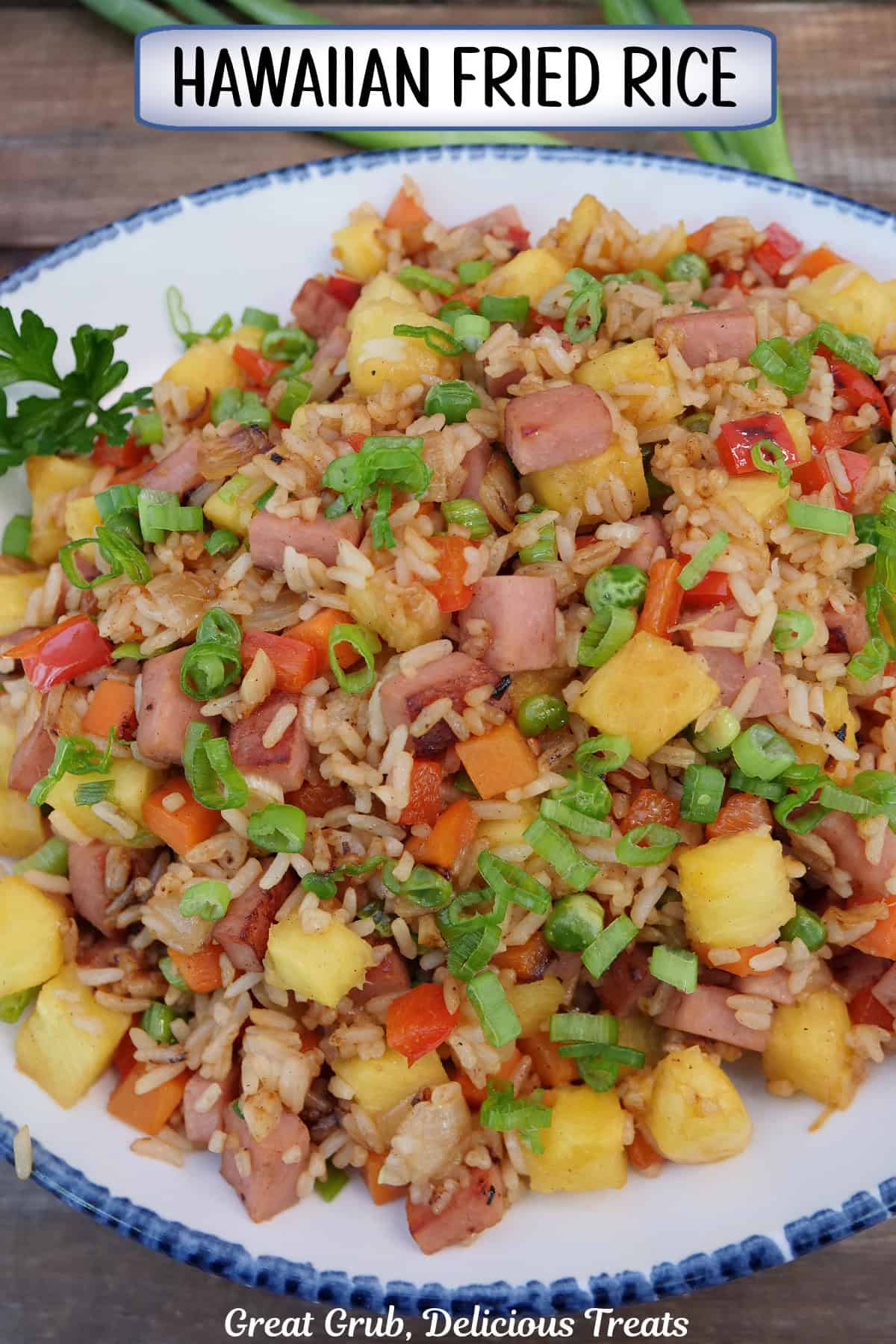 A wood surface with a white bowl with blue trim filled with Hawaiian fried rice with pineapple and Spam.