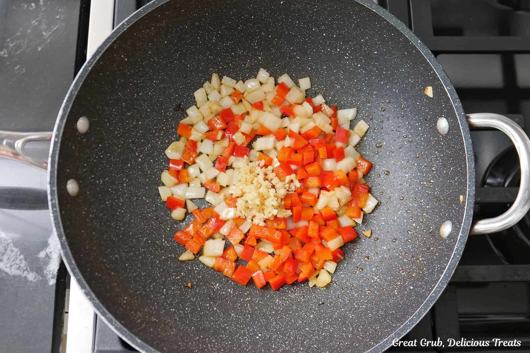 A wok with sauteed onions, peppers, and minced garlic.
