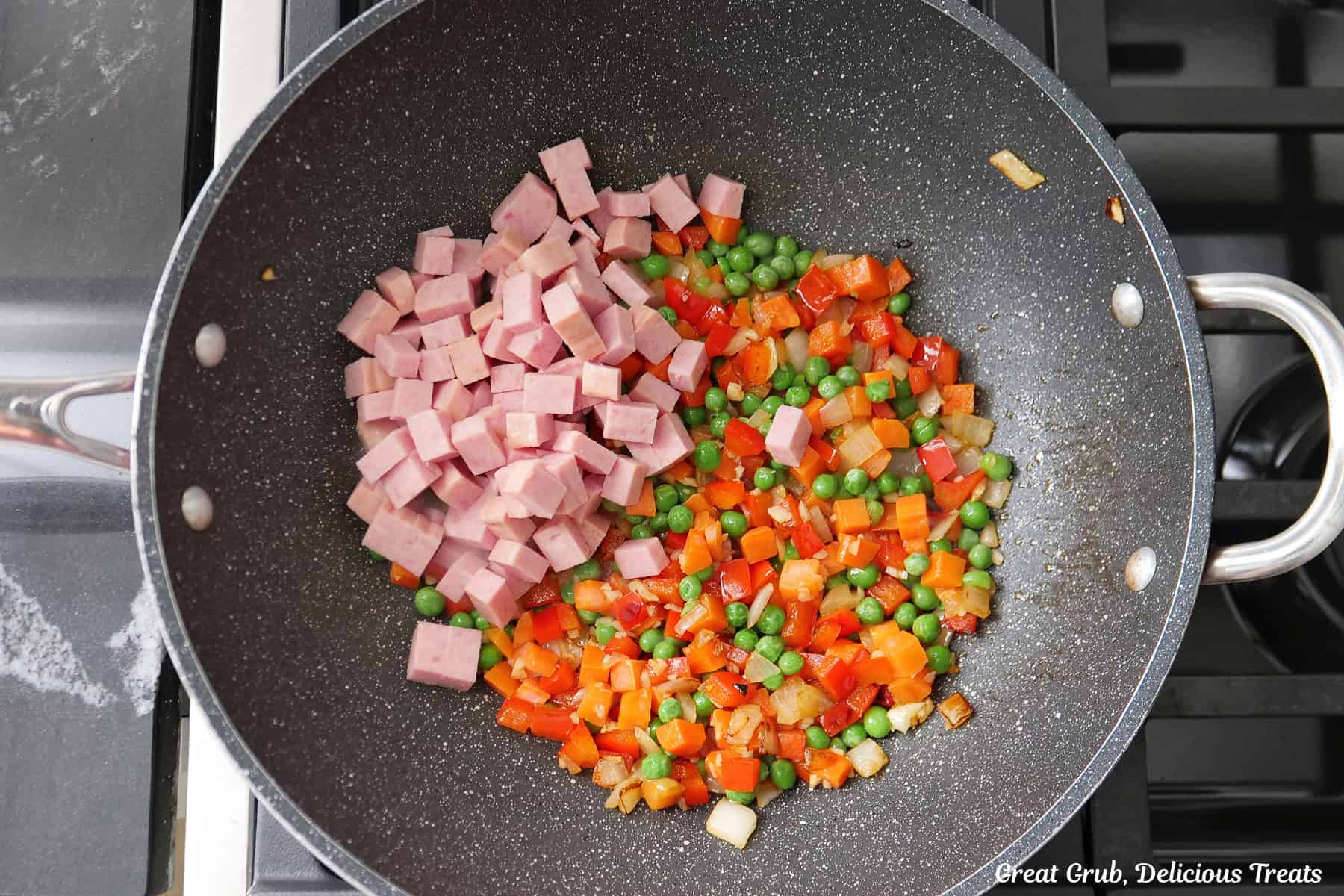 A wok with sauteed onions, peppers, garlic, and diced Spam added to it.