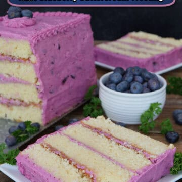 A wood surface with a white plate with a slice of a four layer lemon cake with blueberry frosting on it with the cake and another slice in the background.