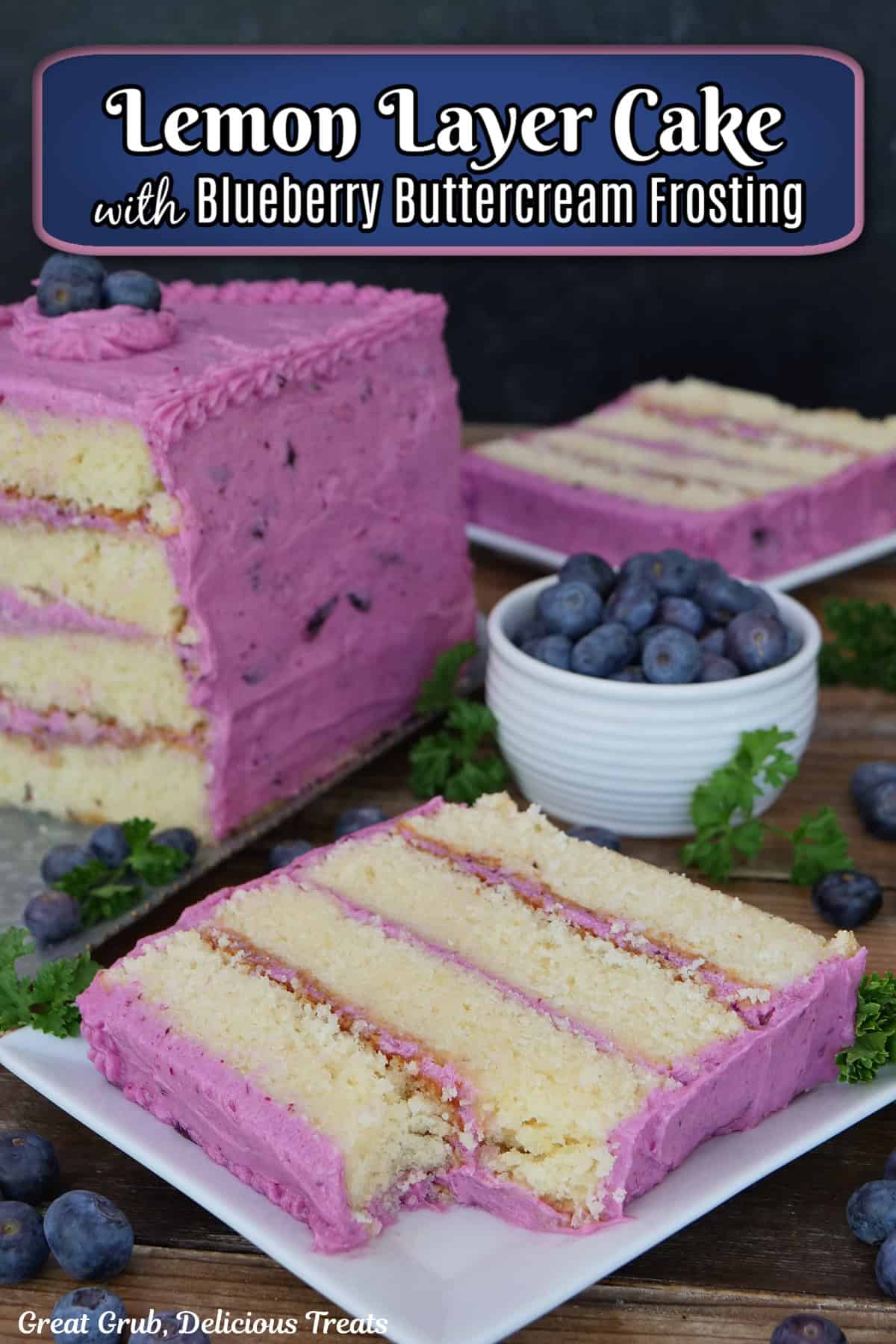 A wood surface with a white plate with a slice of a four layer lemon cake with blueberry frosting on it with the cake and another slice in the background.