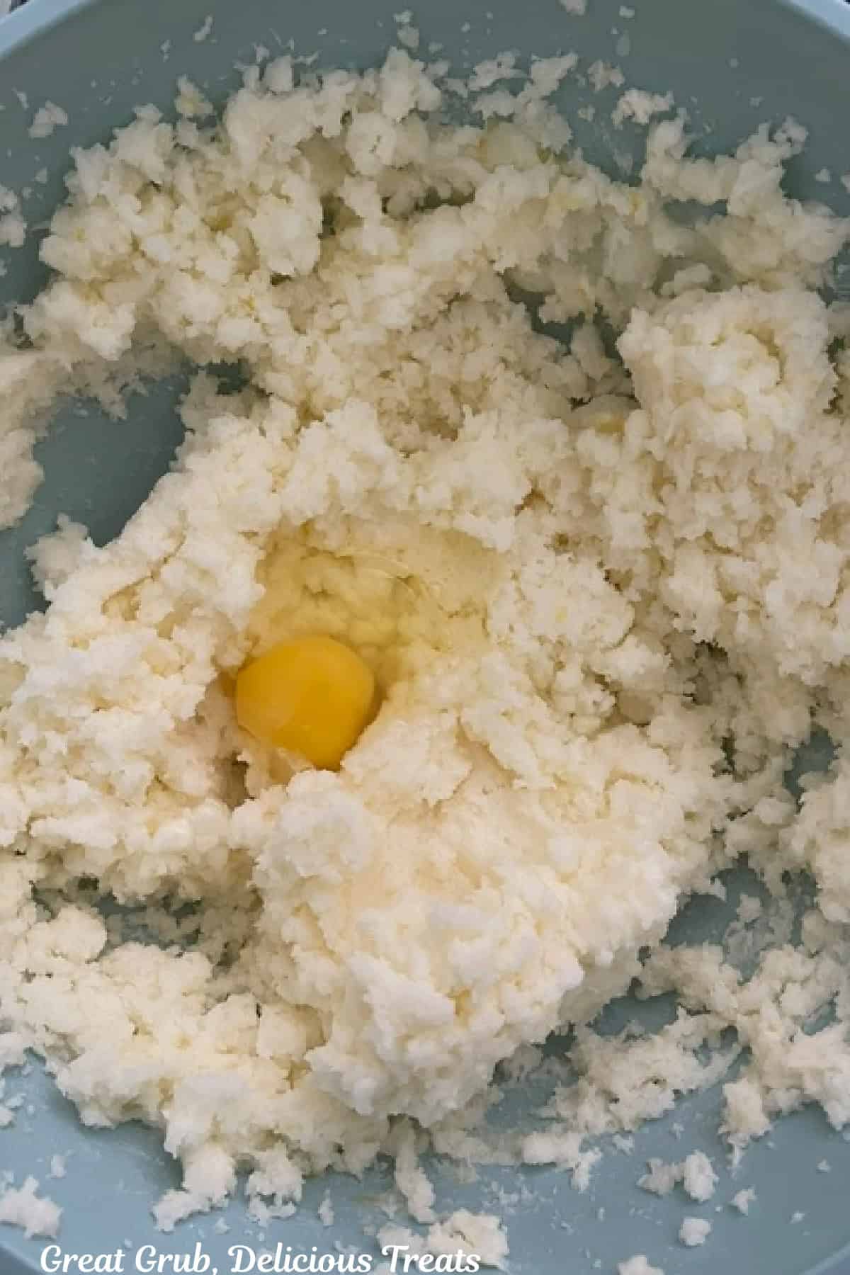 A light blue bowl with creamed butter and an egg in it.