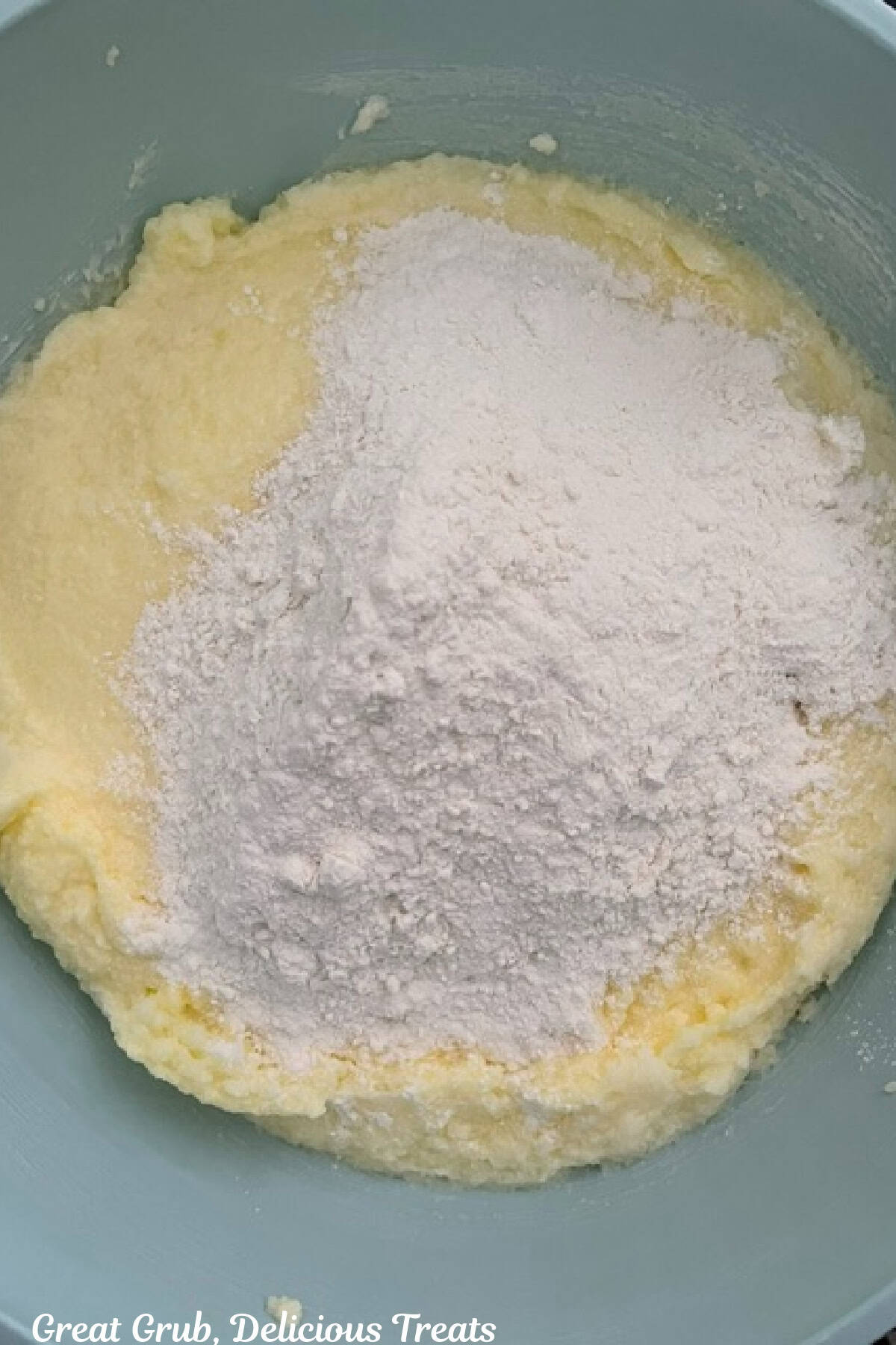 A light blue bowl with dry ingredients being added to wet ingredients of a lemon cake batter.