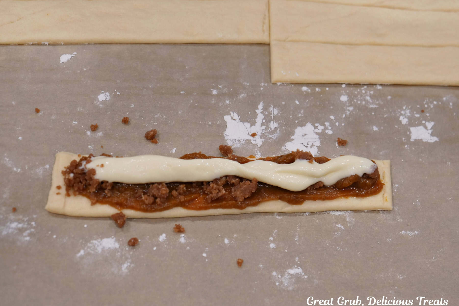 A crescent roll strip of dough with pumpkin filling, streusel, and cream cheese layered on it.
