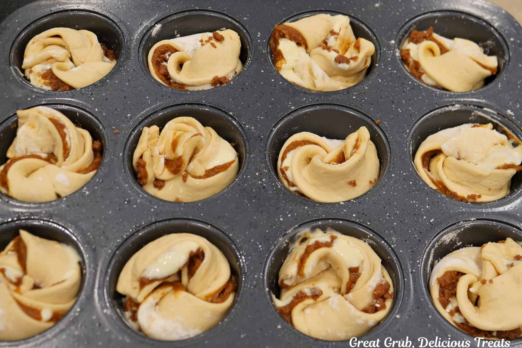 A muffin tin with twelve pumpkin streusel cream cheese muffins in it before being baked.