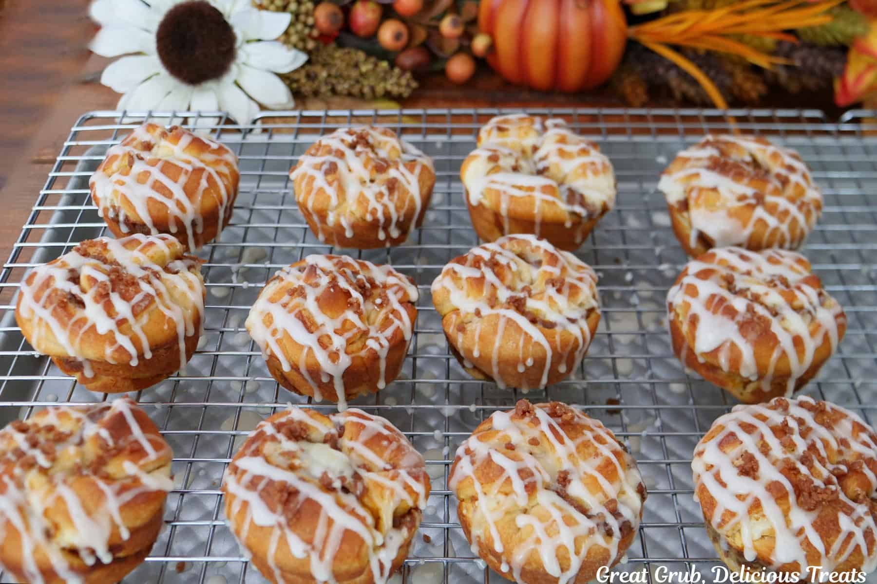A wire rack with twelve baked pumpkin streusel cream cheese muffins on it that have been drizzled with a simple glaze.