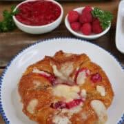 A white plate with blue trim with a round large croissant on it filled with a cheesecake layer and raspberry filling, and a title overlay at the top.