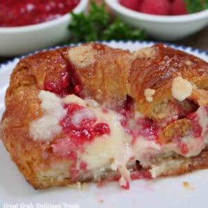 A white plate with blue trim with a large raspberry cream cheese croissant that is but in half on it.