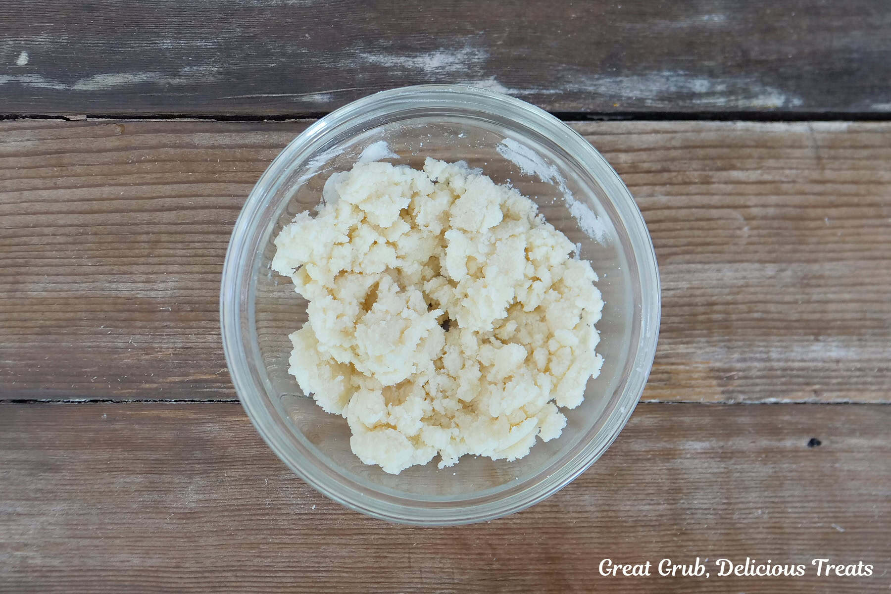 A wood surface with a glass bowl filled with the crumb topping ingredients in it.
