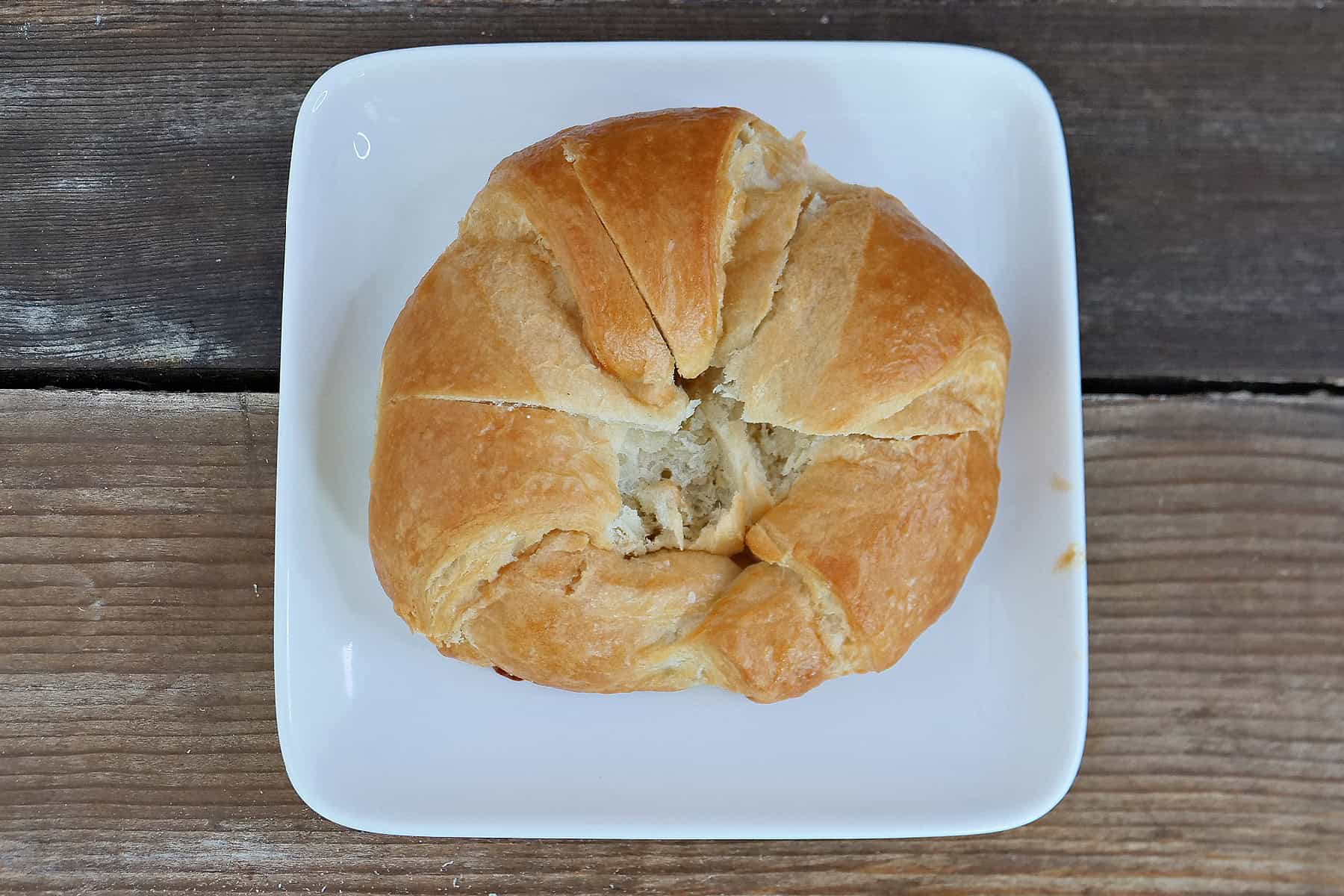 A white square plate with a large store-bought croissant on it with an "X" cut into the top.