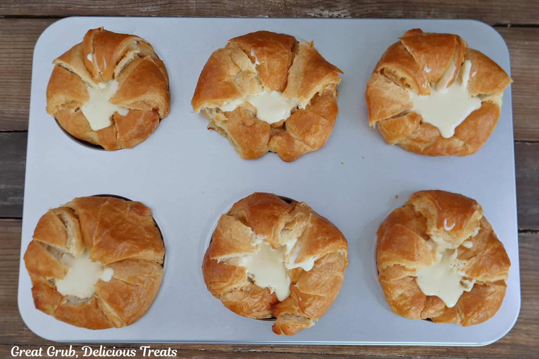 A silver baking sheet with six croissants on it and each one is filled with a cream cheese mixture.
