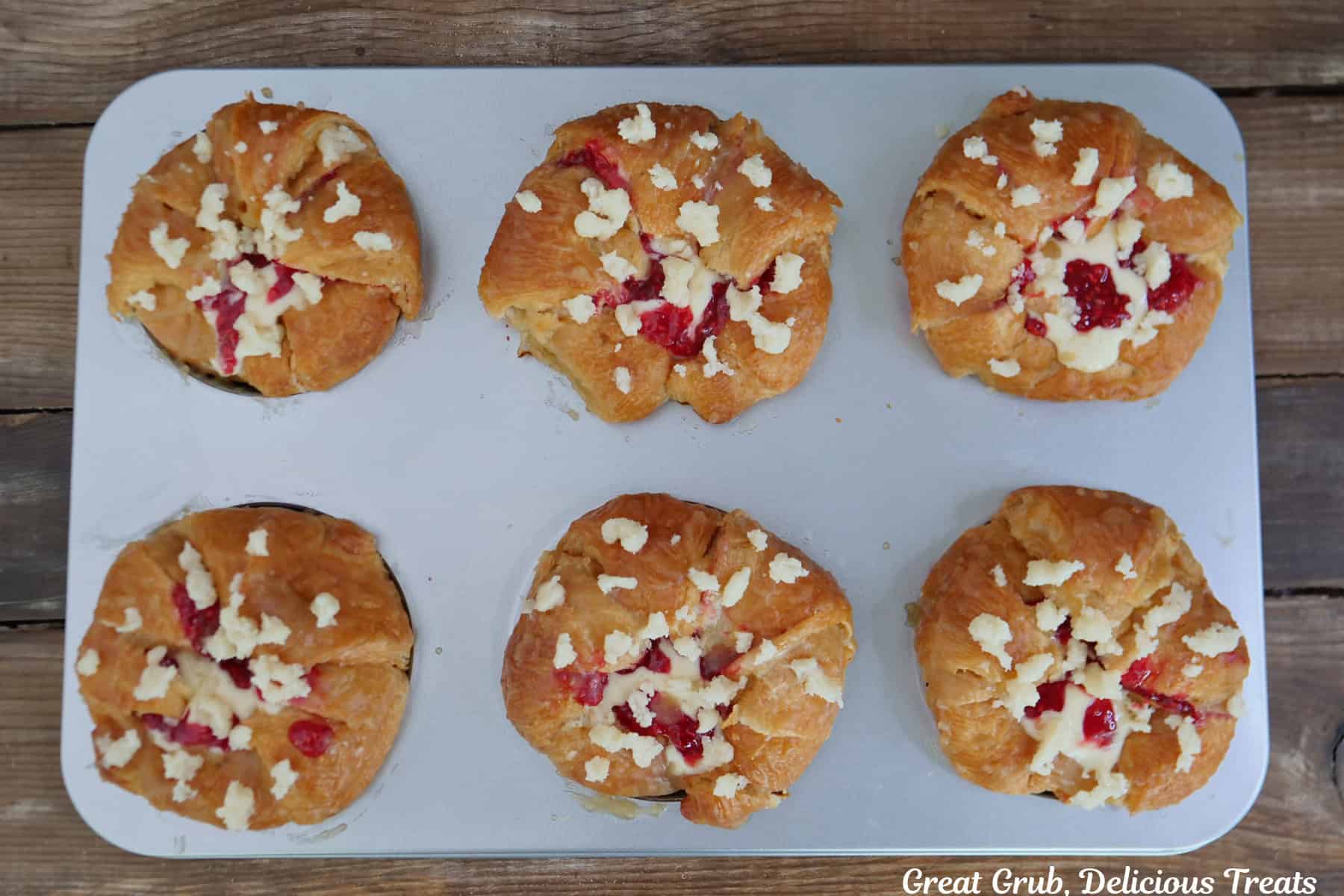 A silver baking sheet with six raspberry cream cheese croissants on it ready to go into the oven.