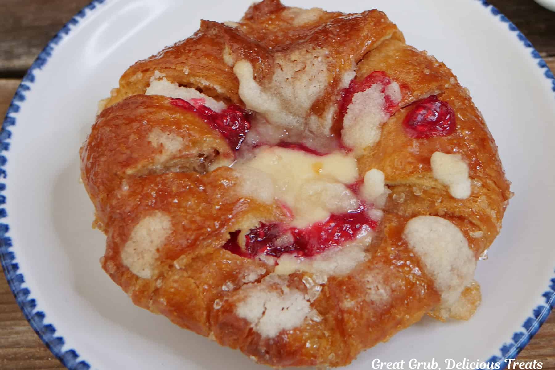 A white plate with blue trim with a raspberry cream cheese croissant on it.