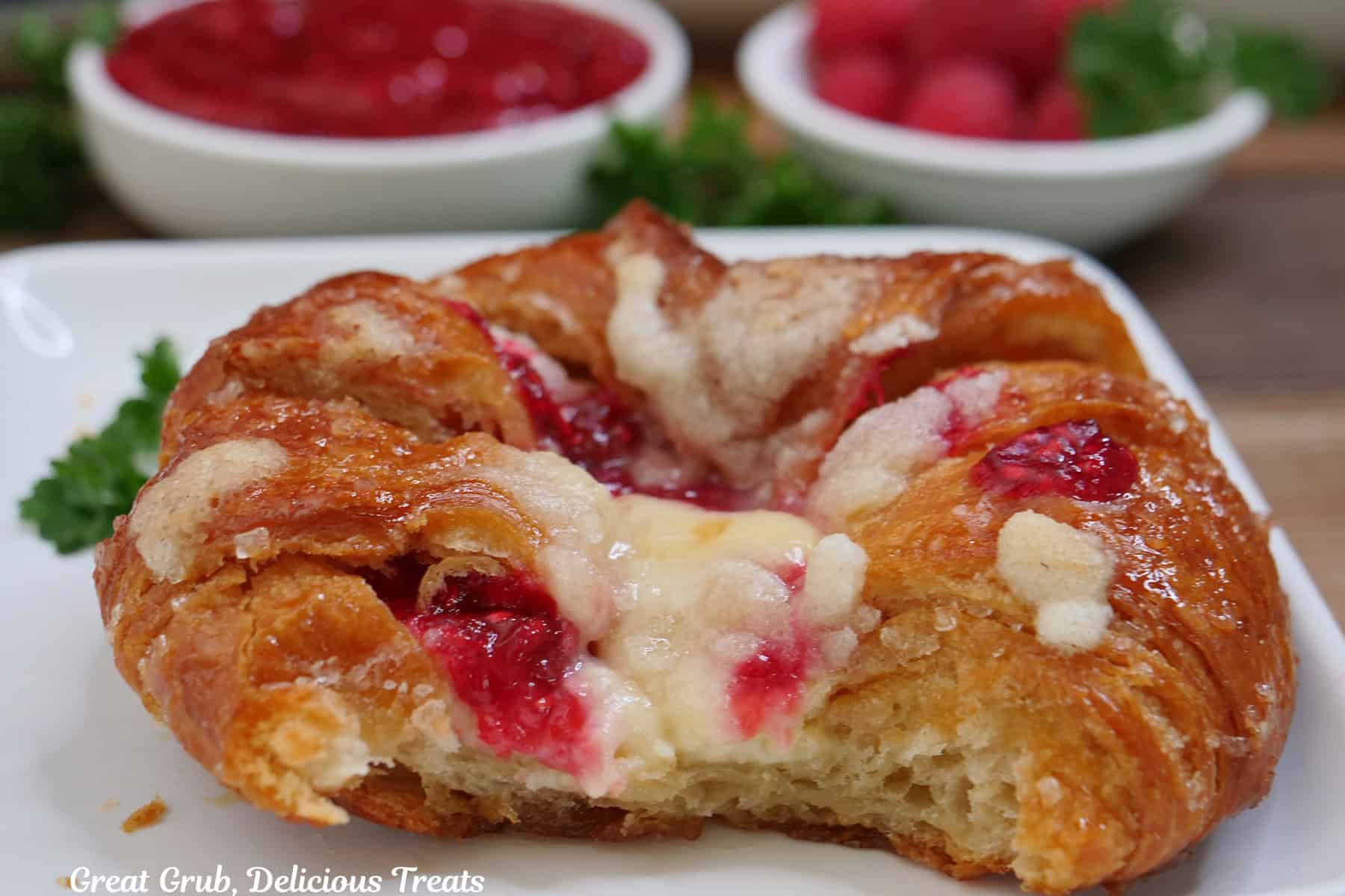 A white plate with blue trim with a large croissant on it filled with a cheesecake and raspberry layer, and a couple bites taken out of it.