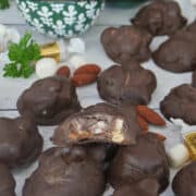 A white surface with homemade chocolate covered rocky road clusters placed randomly all over and a bite taken out of one of the clusters, and a title overlay at the top.