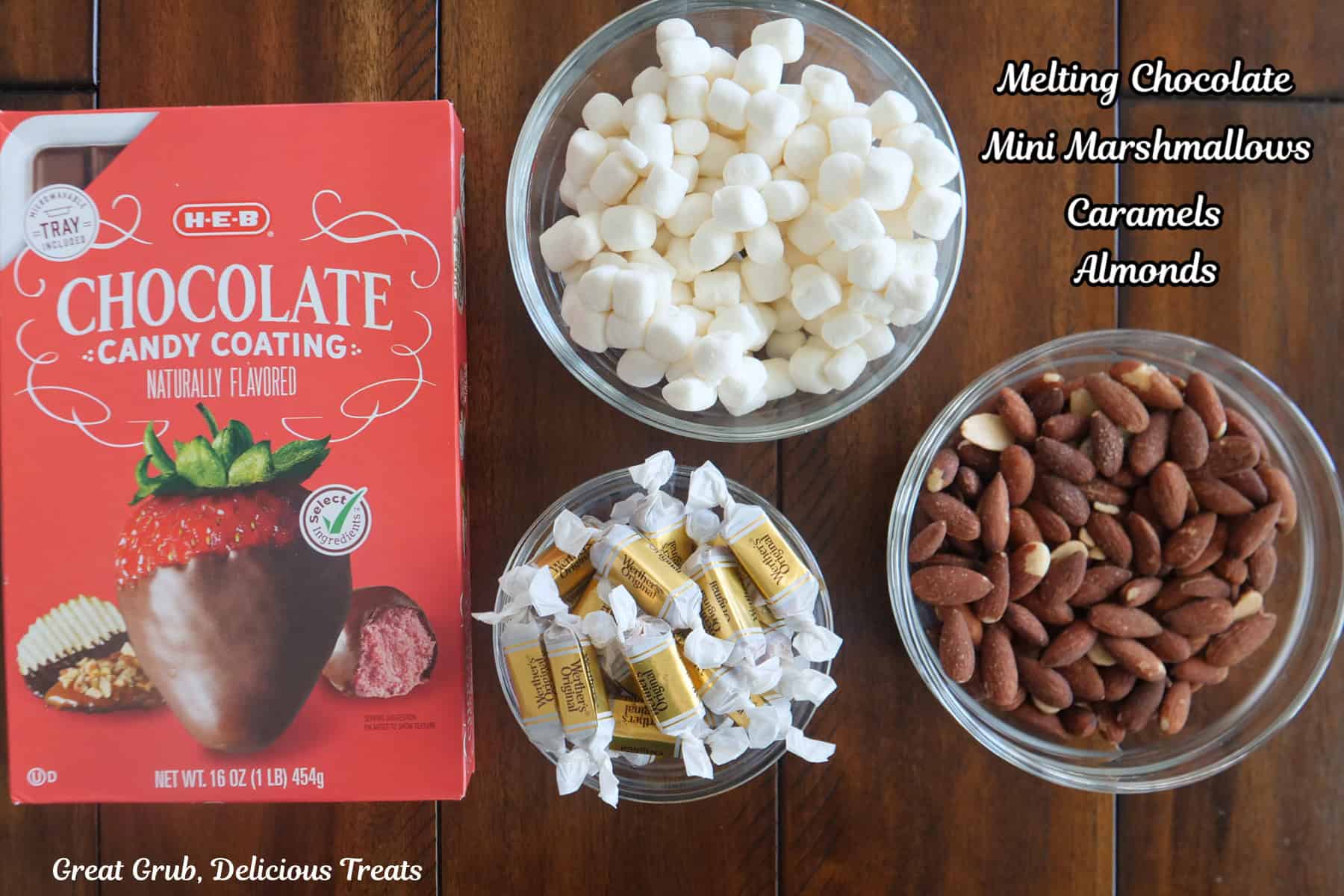 A wood surface with the four ingredients placed on it that are needed to make rocky road clusters.