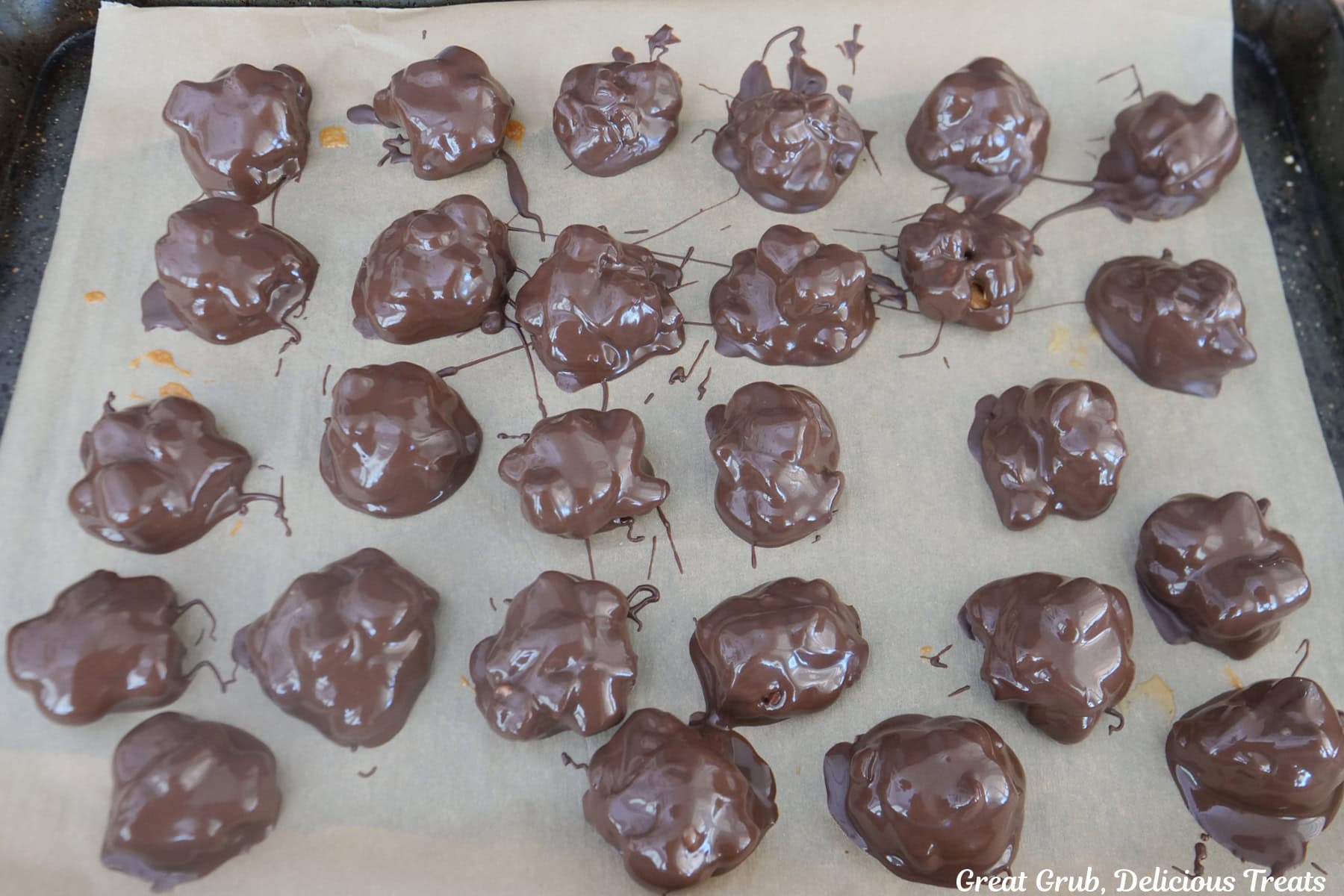 A parchment lined baking sheet with twenty-seven chocolate covered rocky road clusters placed on it for the chocolate to set up and harden.